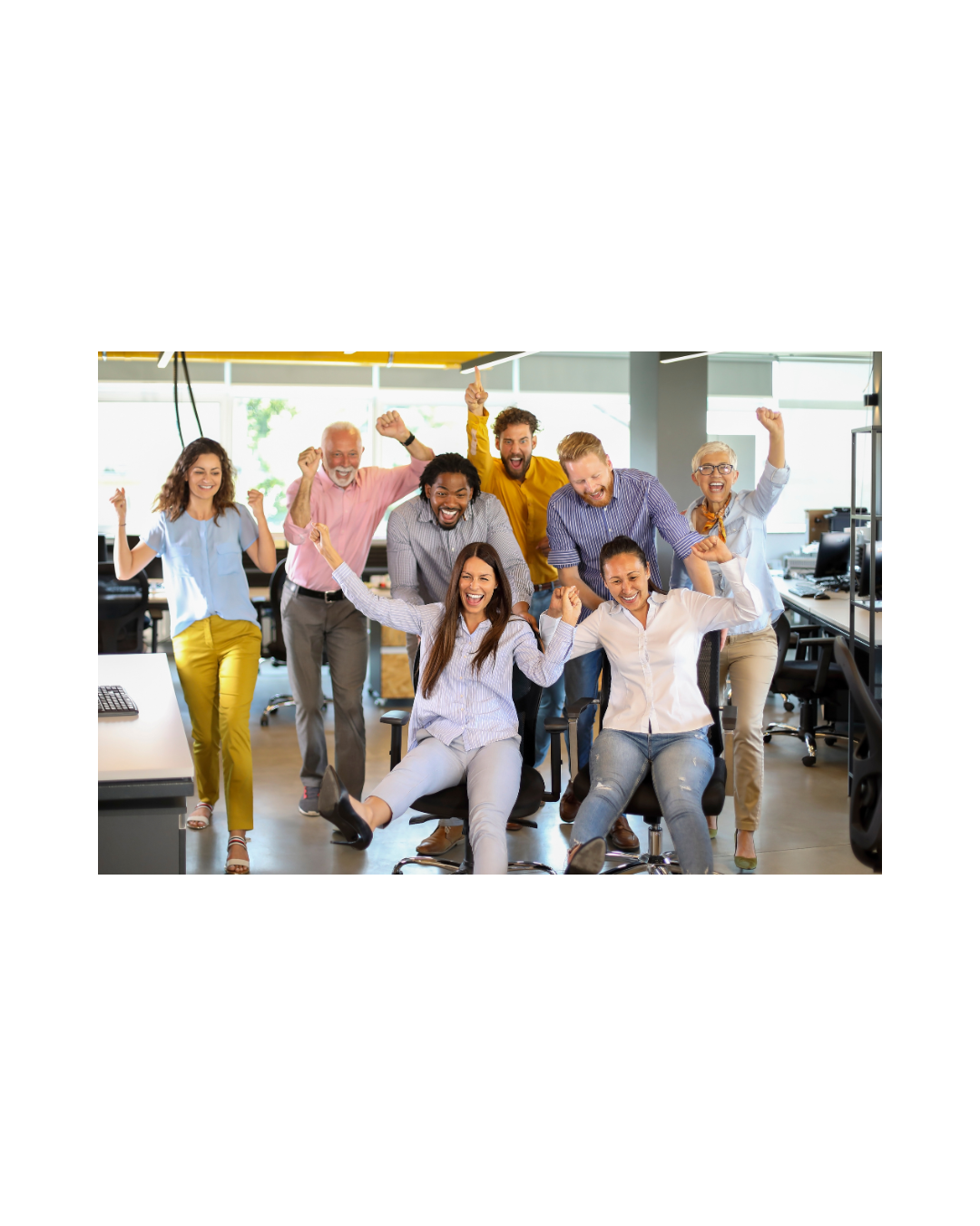 Group of diverse coworkers celebrating and cheering in an office, with some sitting and some standing.