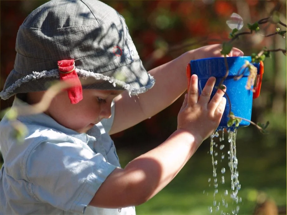 A young boy engages in sensory play with water and a bucket.