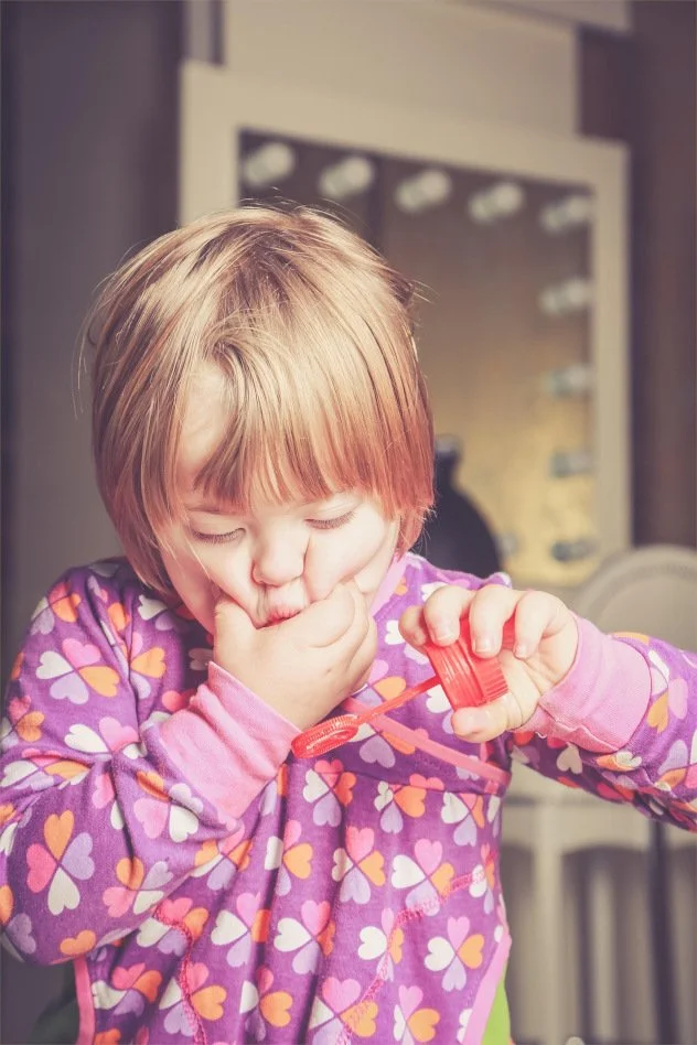 A young girl plays with bubbles while supporting her mouth with her hand.