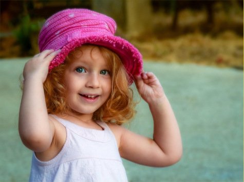 A girl playfully adjusts her pink hat.