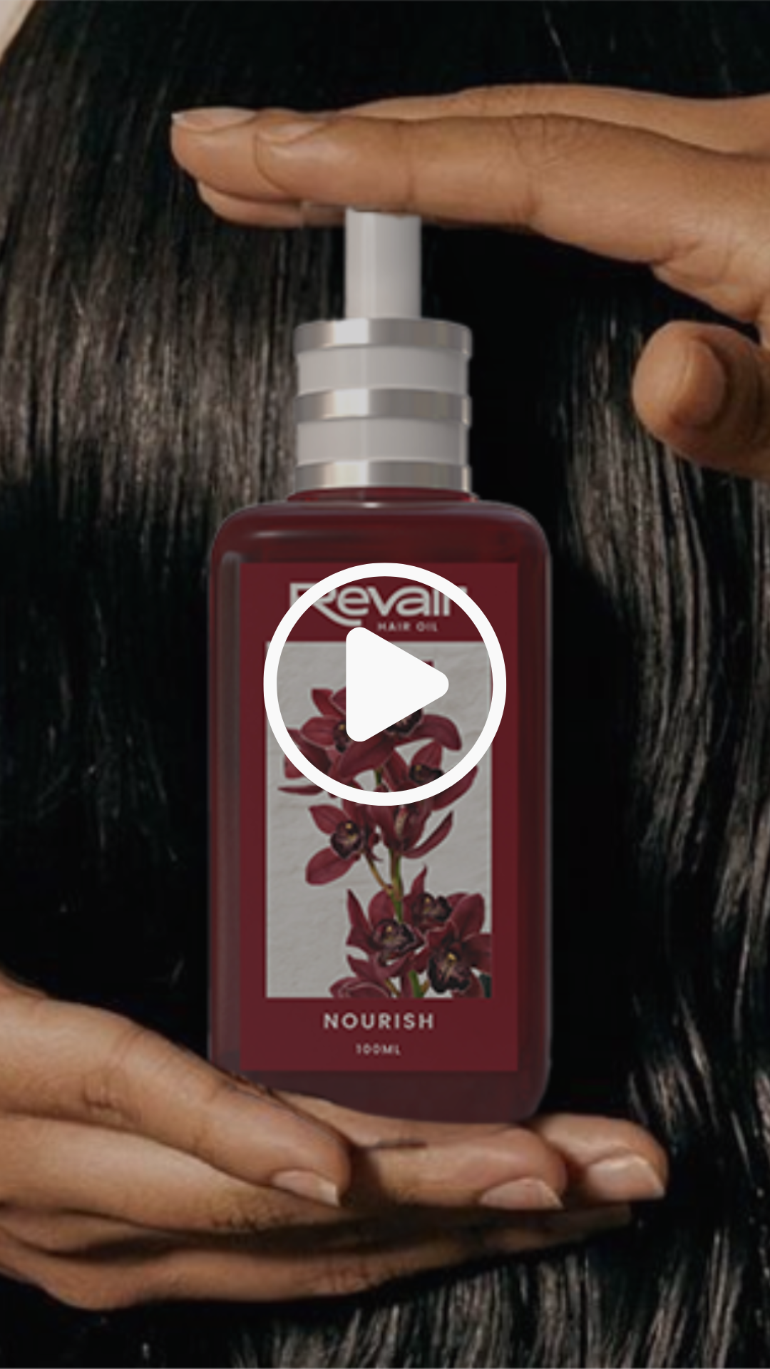 A person holding a bottle of Revlon Nourish hair oil with a floral label featuring red and black flowers against a dark background.