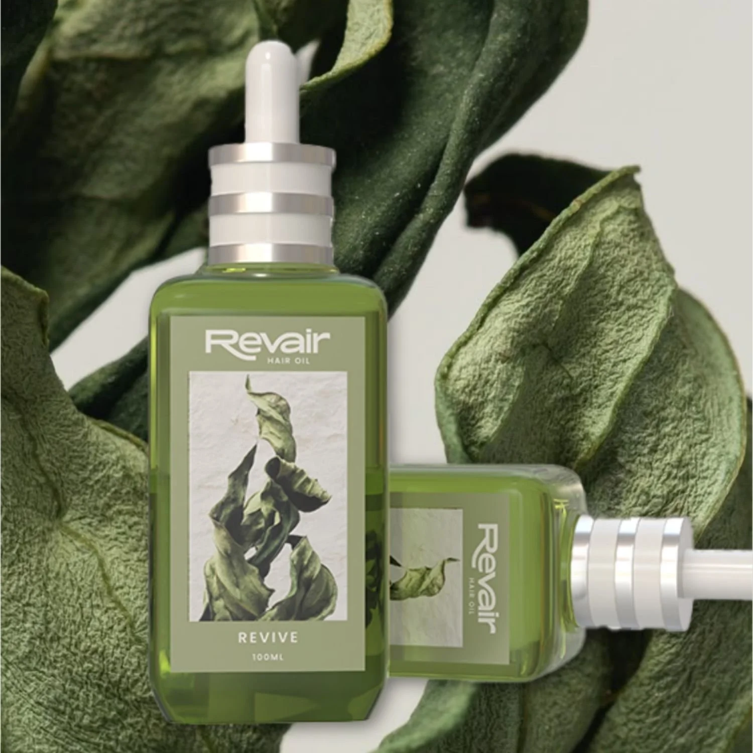 Two bottles of Revair hair oil placed on green leaves with a textured background.