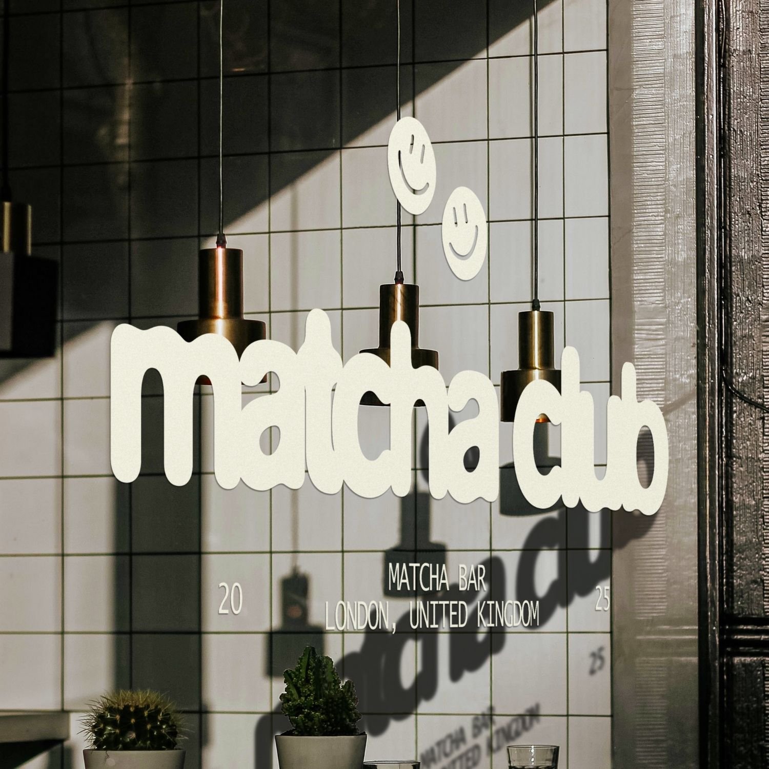 Sign for MΔTCHABatch restaurant at a matcha bar in London, United Kingdom, with hanging smiley face decorations and small potted plants below.