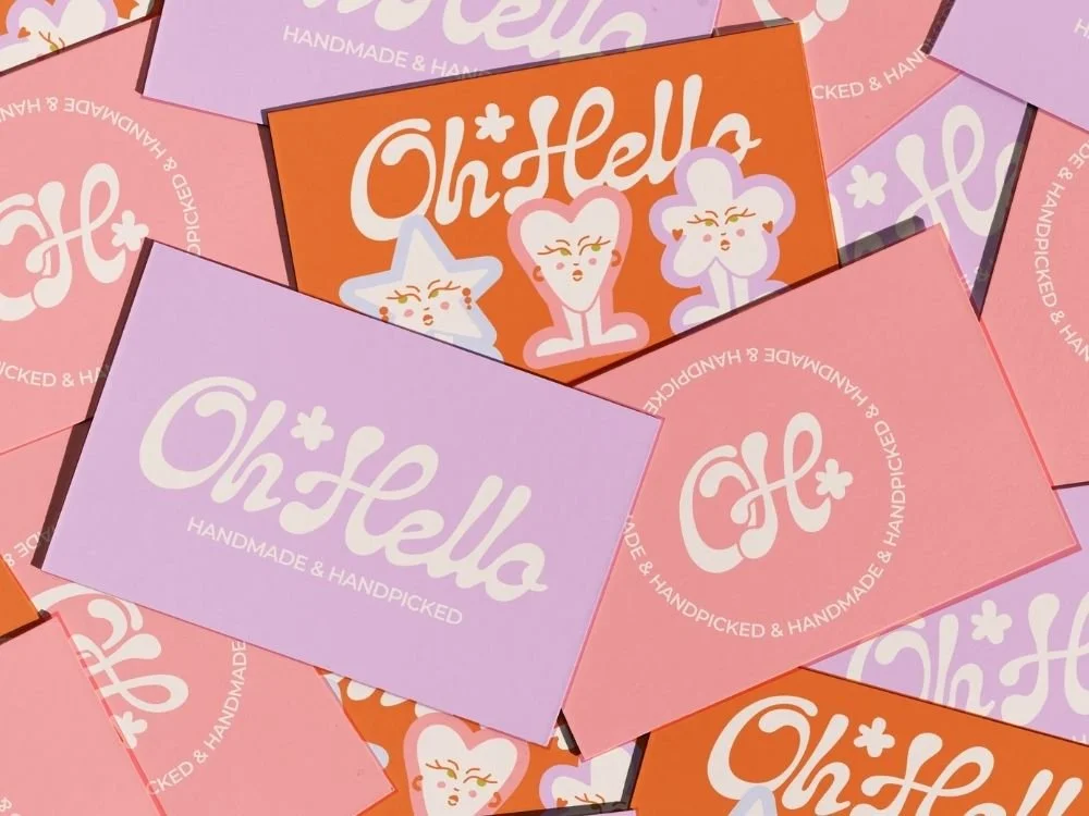 Multiple colorful business cards with the text 'Oh Hello' and 'Handmade & Handpicked'. The cards are pink, purple, and orange, featuring cute character illustrations.
