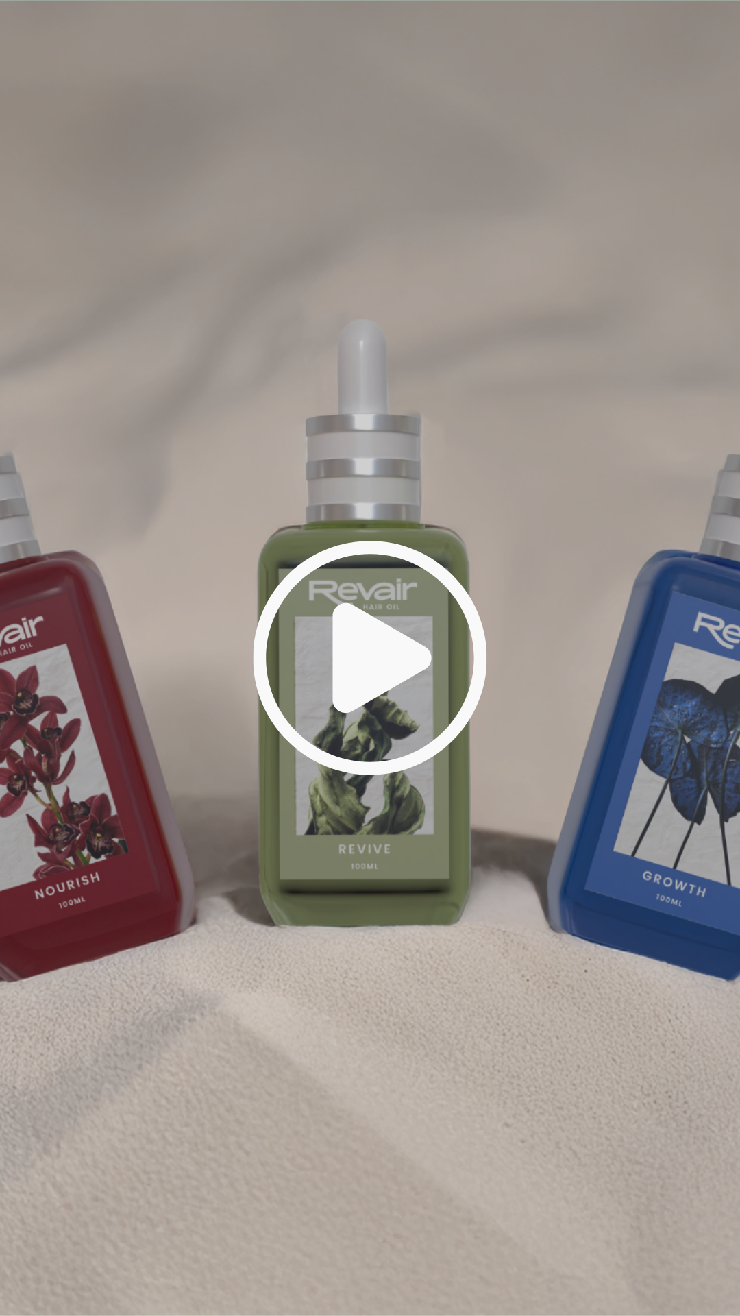 Three bottles of hair oil on a beige fabric surface, with the green bottle in the center labeled 'Revair Revive,' flanked by a red bottle labeled 'Nourish' on the left and a blue bottle labeled 'Growth' on the right.