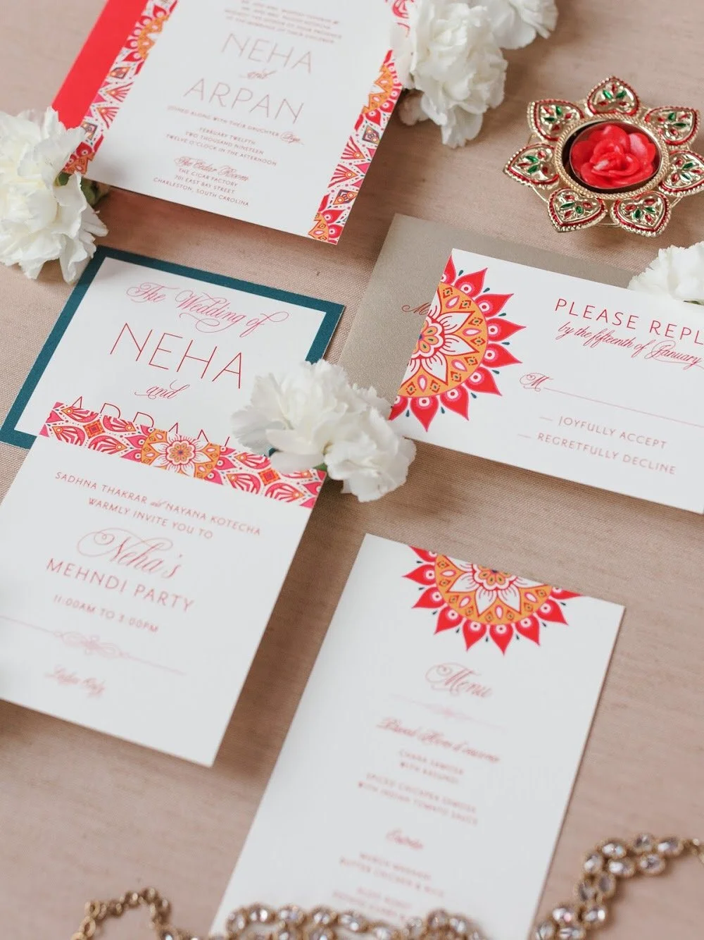 Wedding invitation cards with floral and mandala designs, white flowers, and jewelry on a pink background.