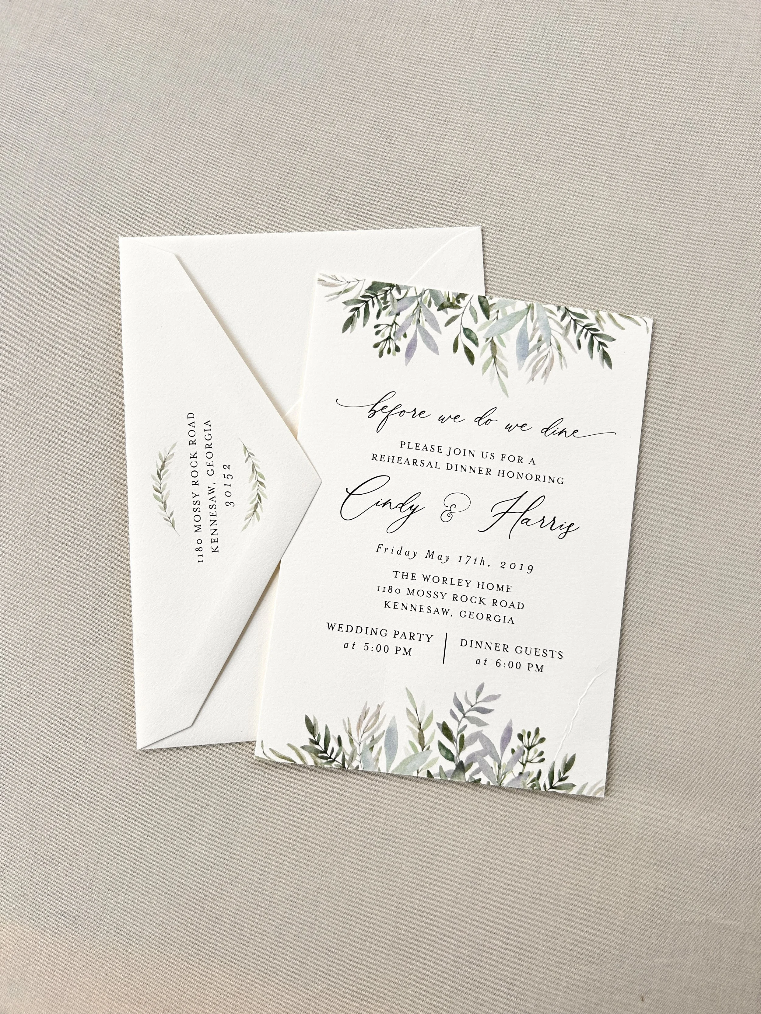 A wedding invitation and matching envelope with a botanical design on a beige surface.