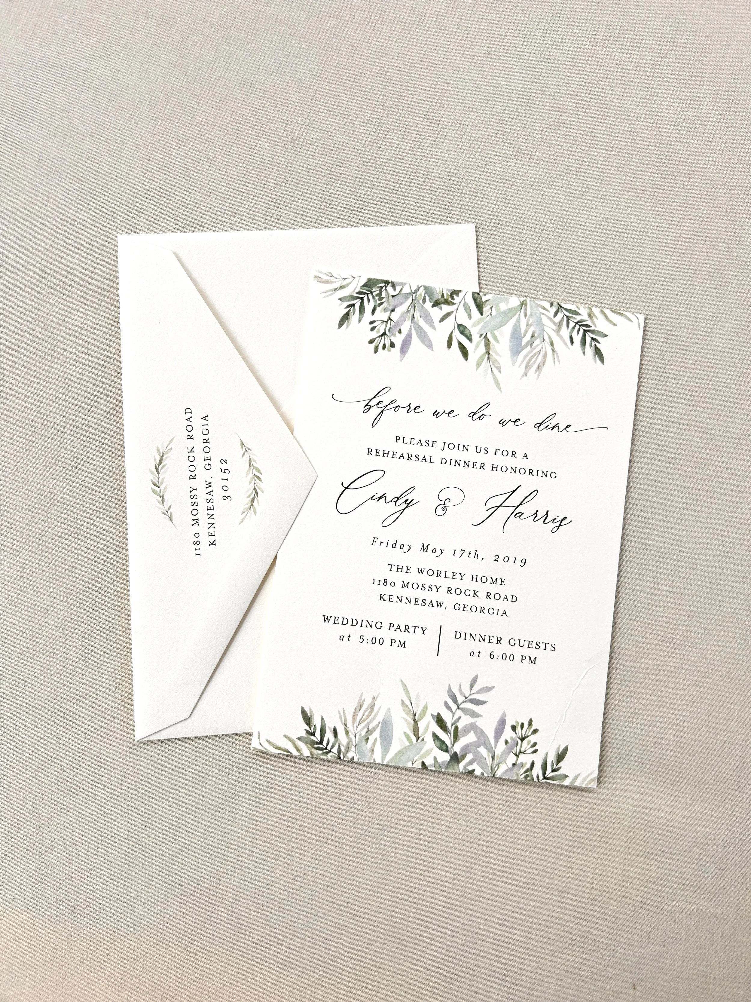 Wedding invitation card with greenery illustrations, and an envelope with address details.