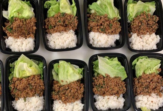 Black meal prep containers filled with rice, ground beef, lettuce, and ground beef.