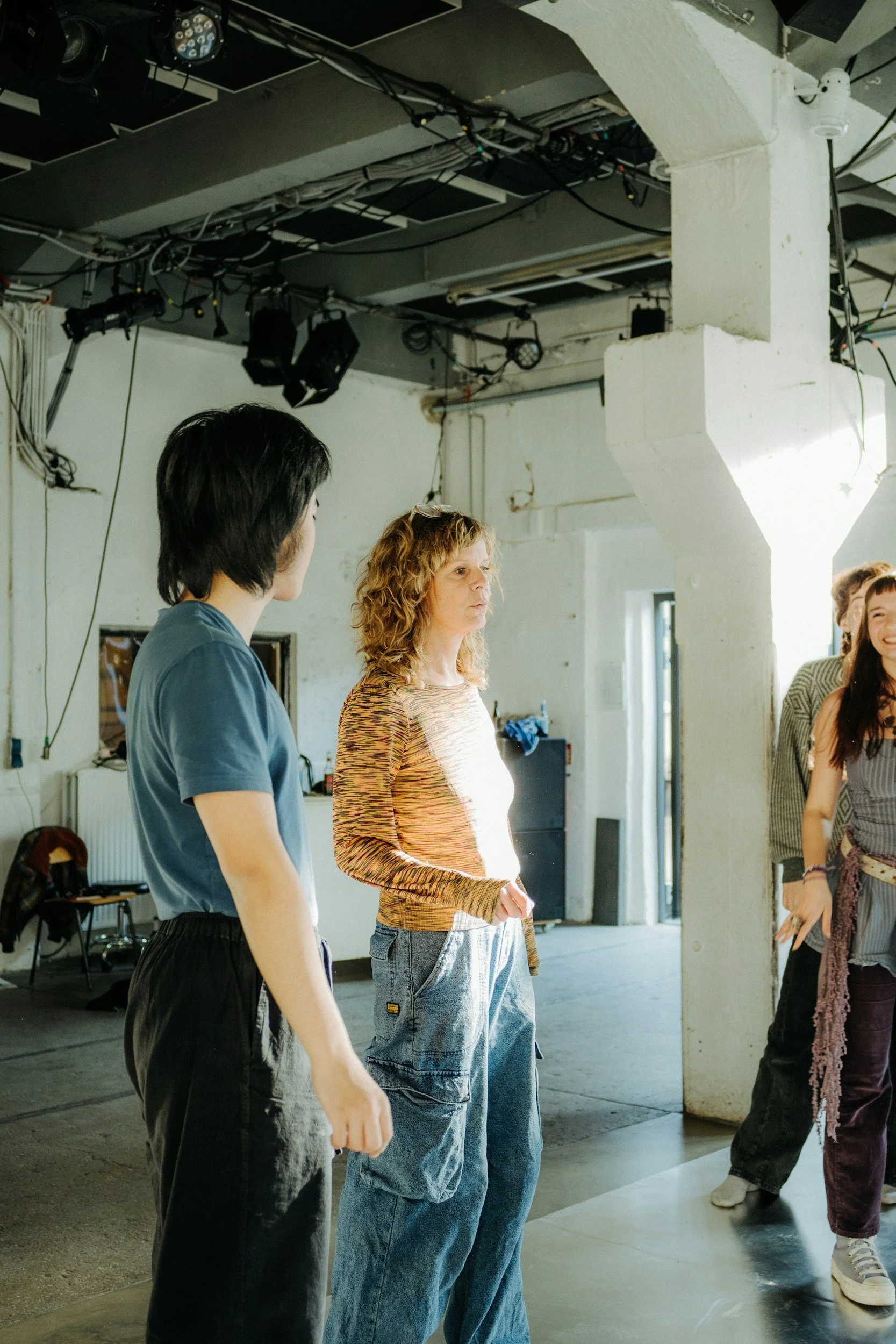 Group of people in an industrial-style room with exposed pipes and lighting equipment, engaging in conversation.