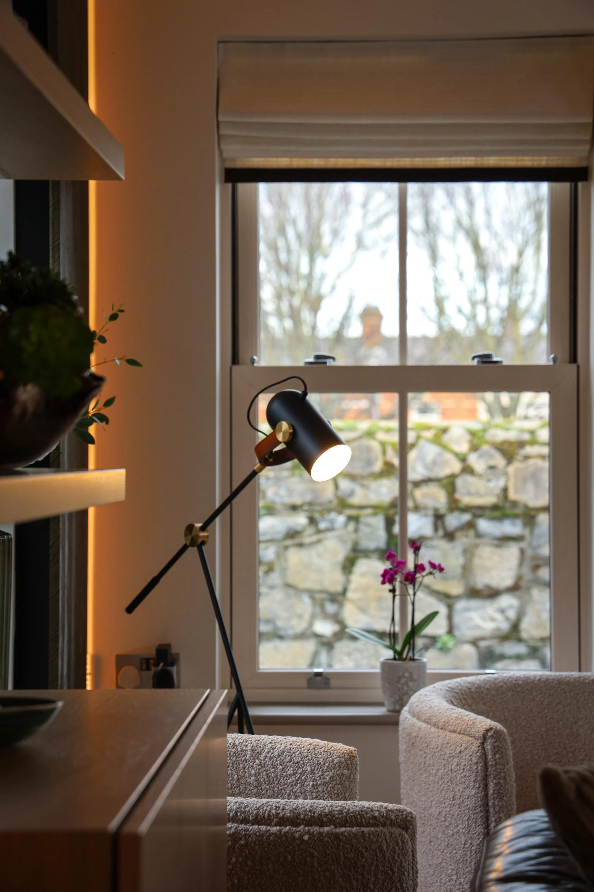 Interior view of a cozy living space focusing on a window with a potted orchid and a small table with a lamp, showcasing a warm and inviting atmosphere.