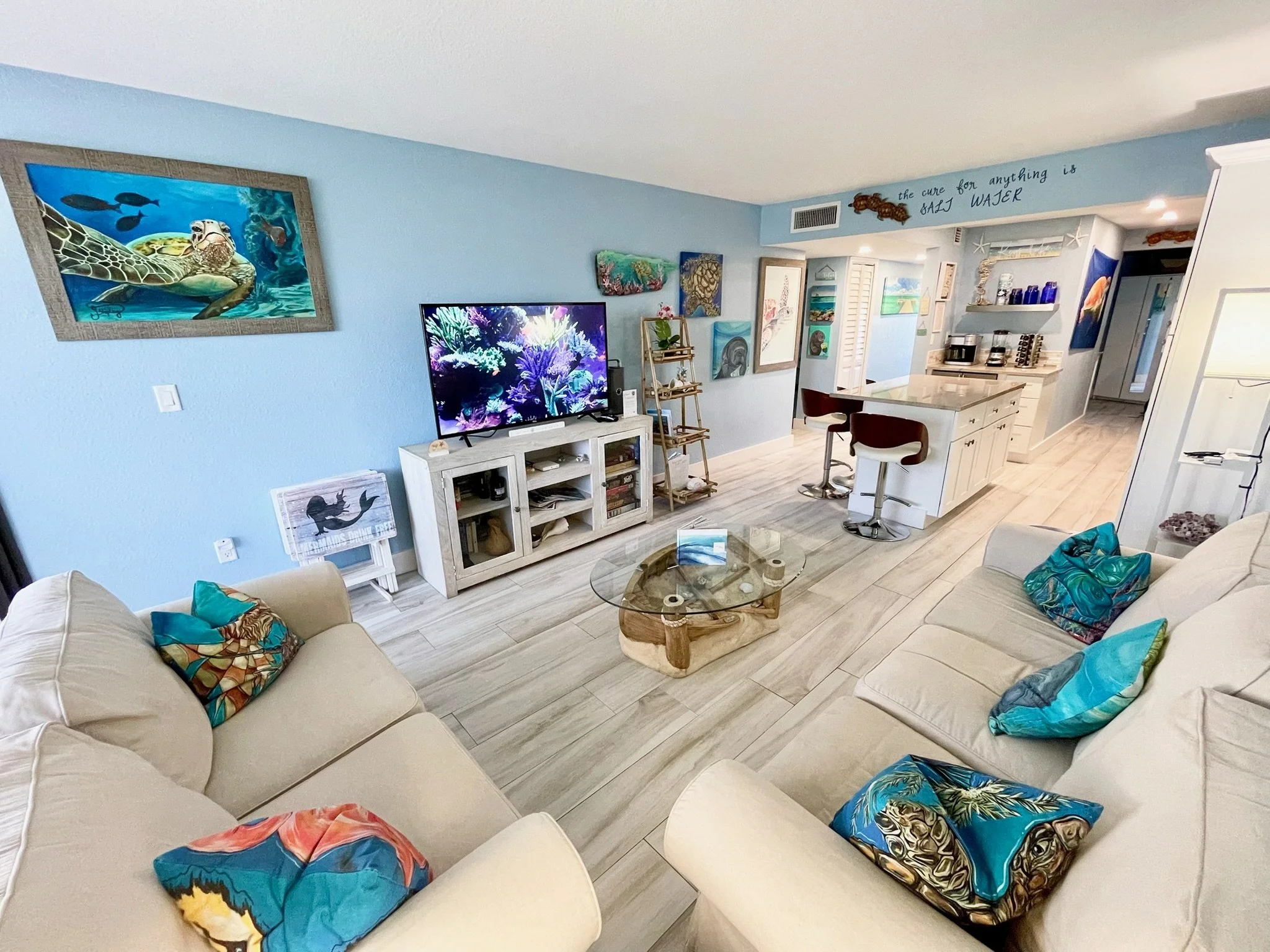 Relax in the open-concept living room at our Moon Bay Key Largo vacation rental, featuring comfortable seating, a Roku TV, local undersea-inspired artwork, board games, books, and a seamless connection to the fully equipped kitchen.