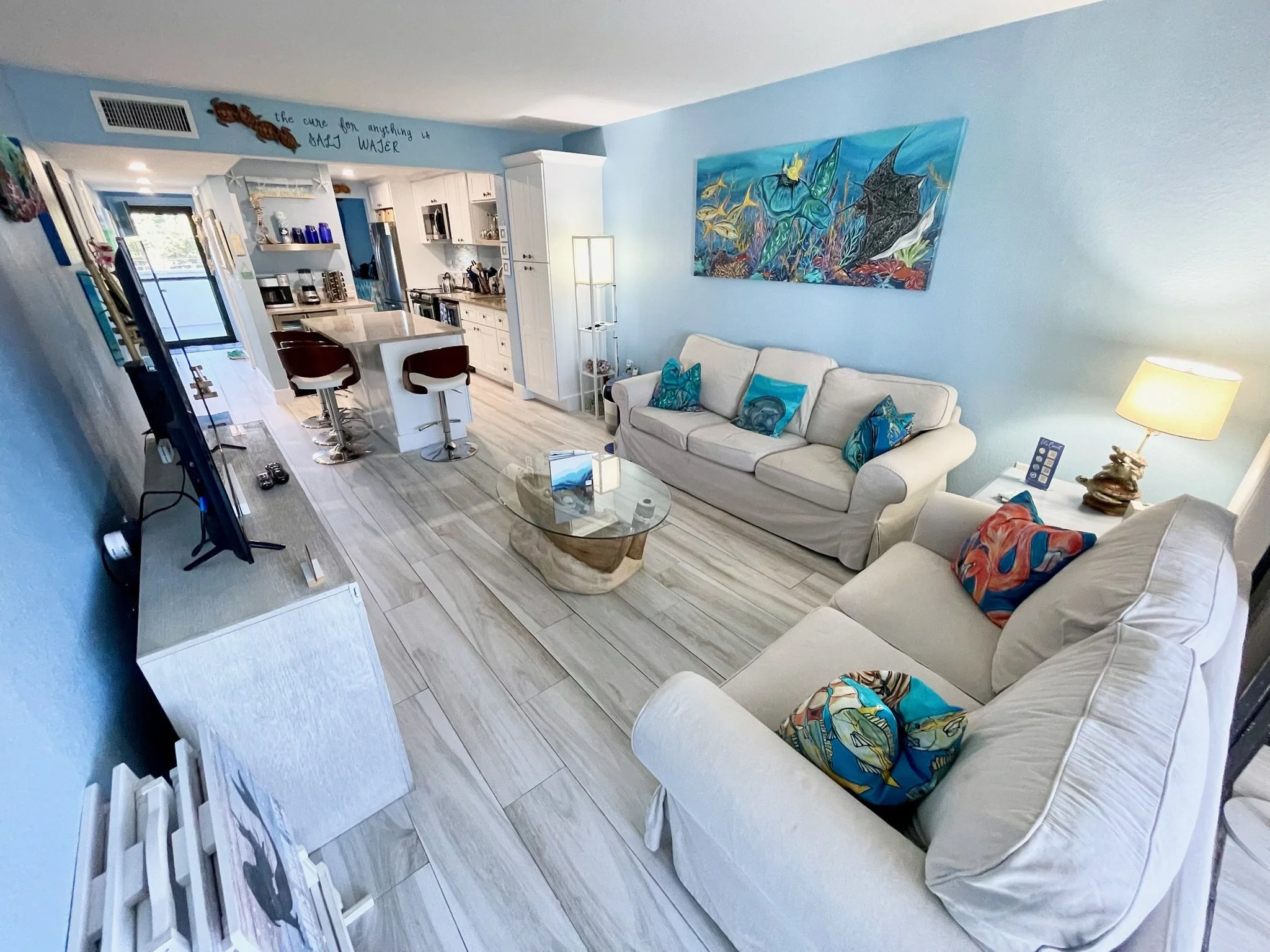 Relax in the open-concept living room at our Moon Bay Key Largo vacation rental, featuring comfortable seating, a Roku TV, local undersea-inspired artwork, board games, books, and a seamless connection to the fully equipped kitchen.