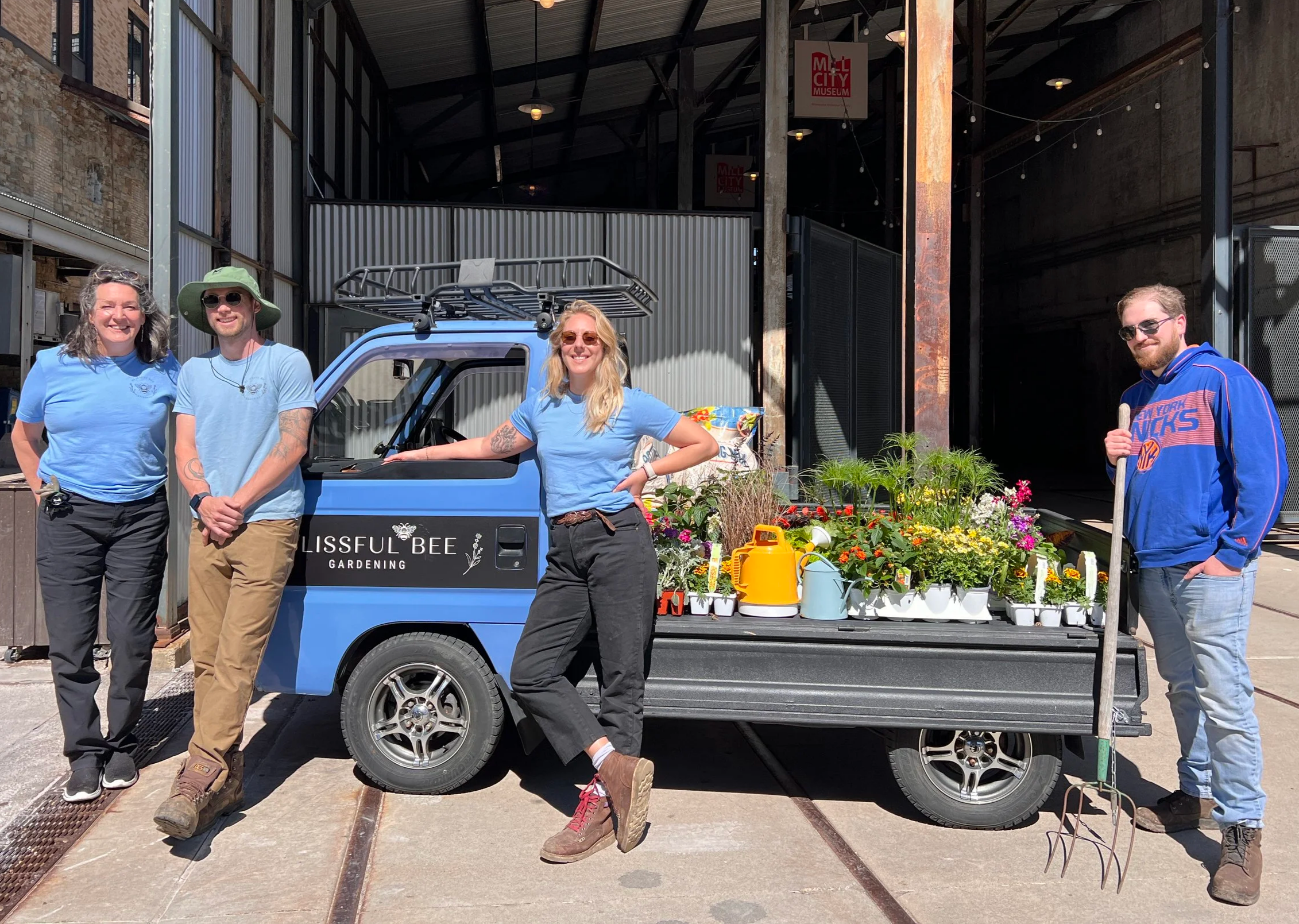 Blissful Bee Gardening team installing decorative pots at Minneapolis farmers market with mini blue kei truck