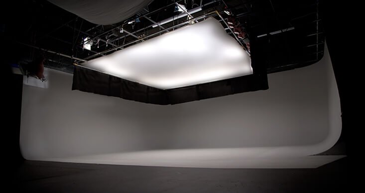 Photo of a professional photography studio with a large white curved backdrop, overhead lighting, and a softbox in the ceiling for shooting photos.