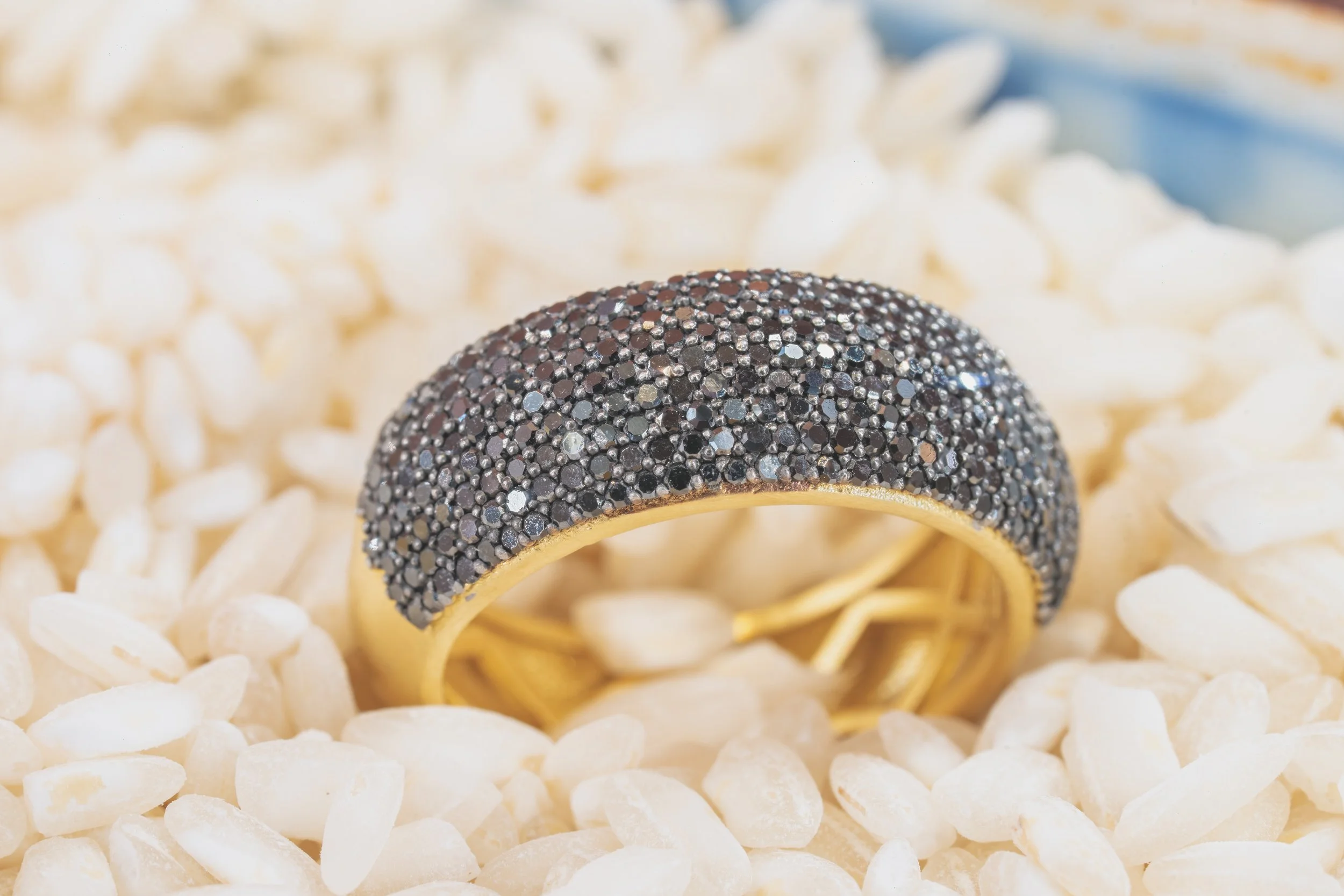 A gold ring encrusted with black and silver diamonds, resting on white rice grains.