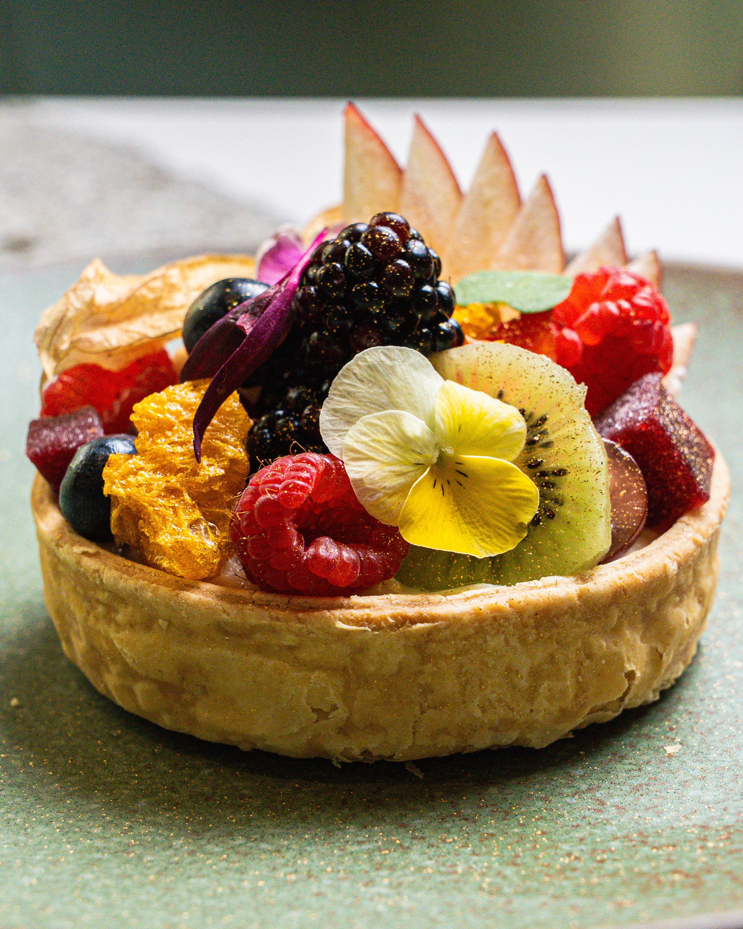 Close-up of a fruit tart with various fresh fruits and edible flowers on top.