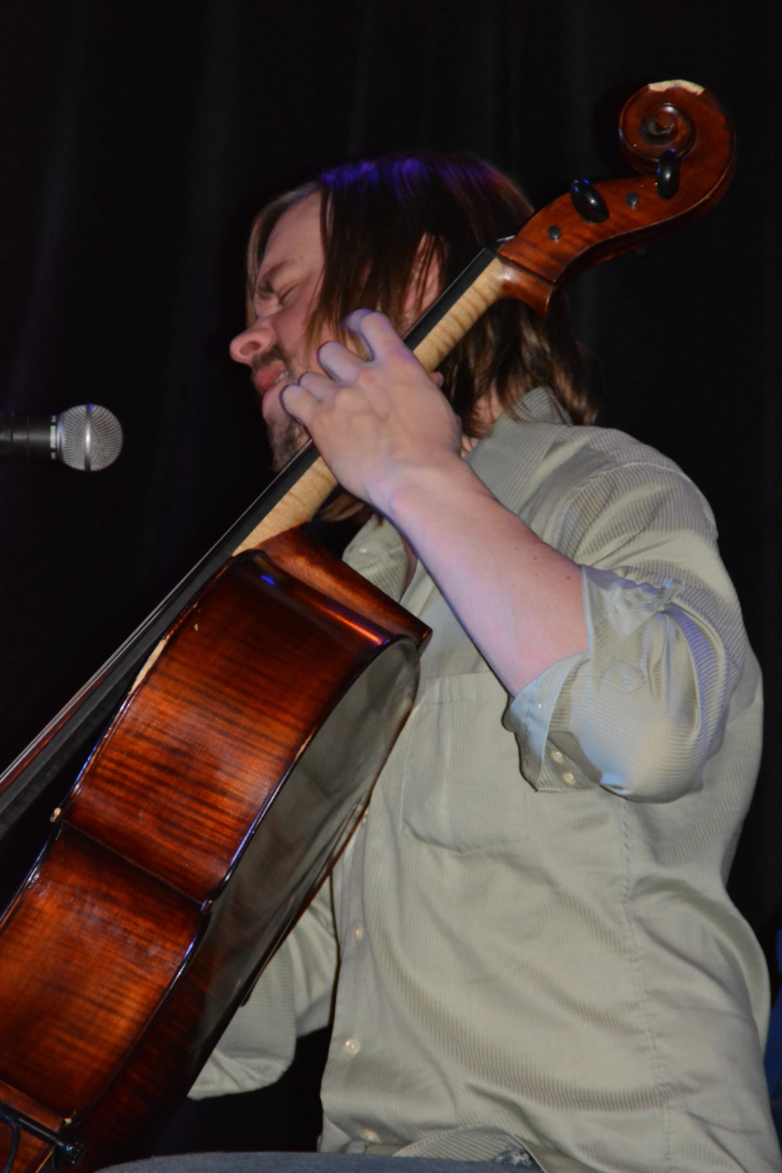 A man with long hair and a beard playing an acoustic guitar and singing into a microphone on a stage.