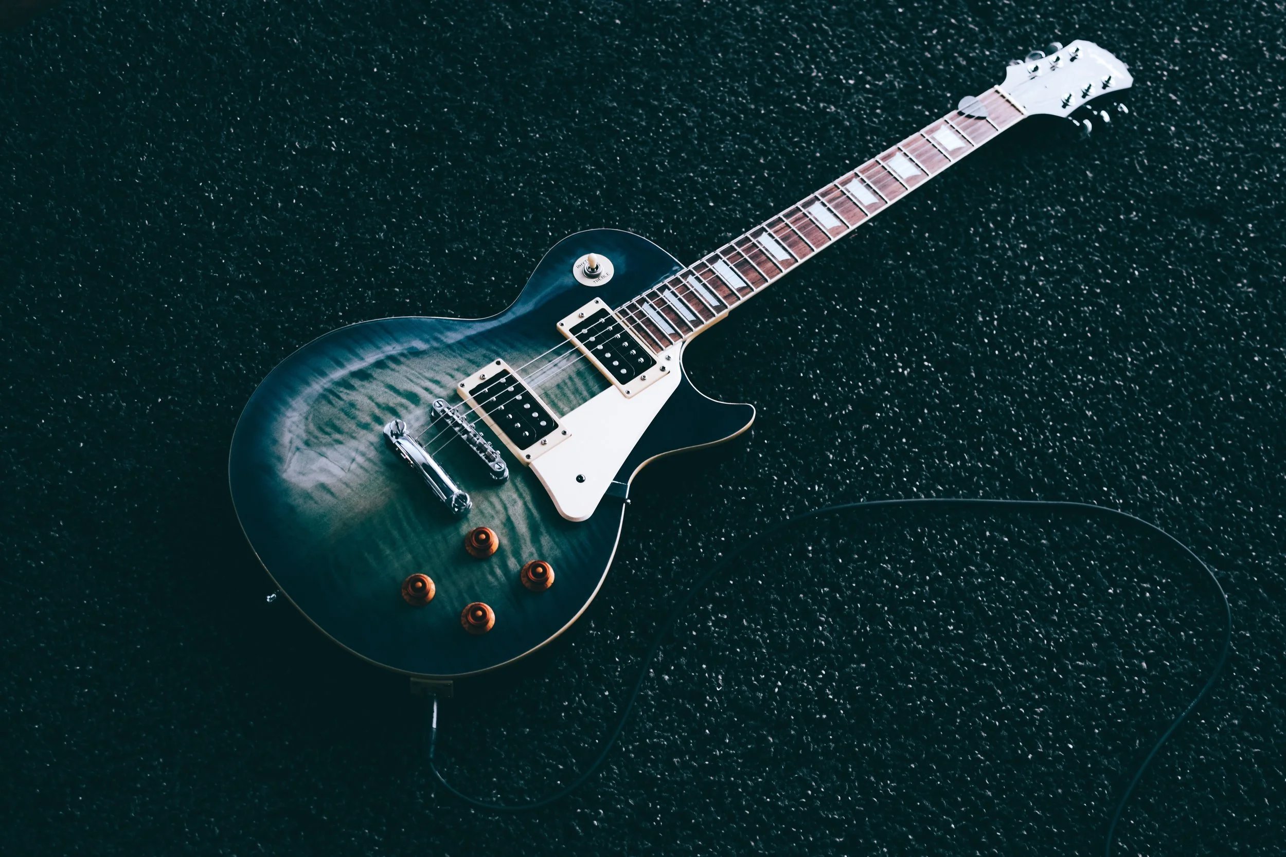Electric guitar with a green and black sunburst finish lying on a black textured surface.
