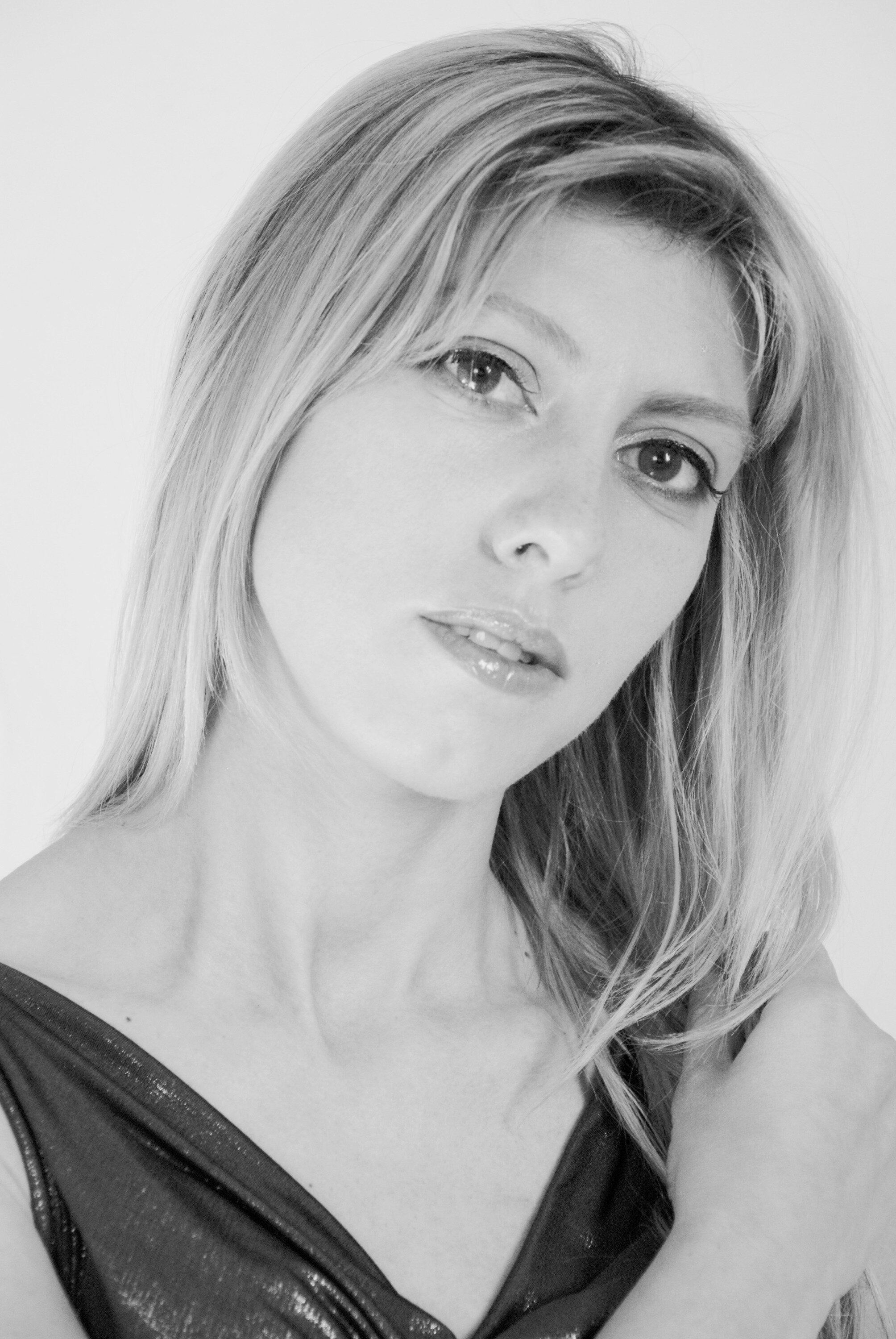 A black and white portrait of a woman with shoulder-length hair, wearing a shiny top, looking at the camera with a slight smile.