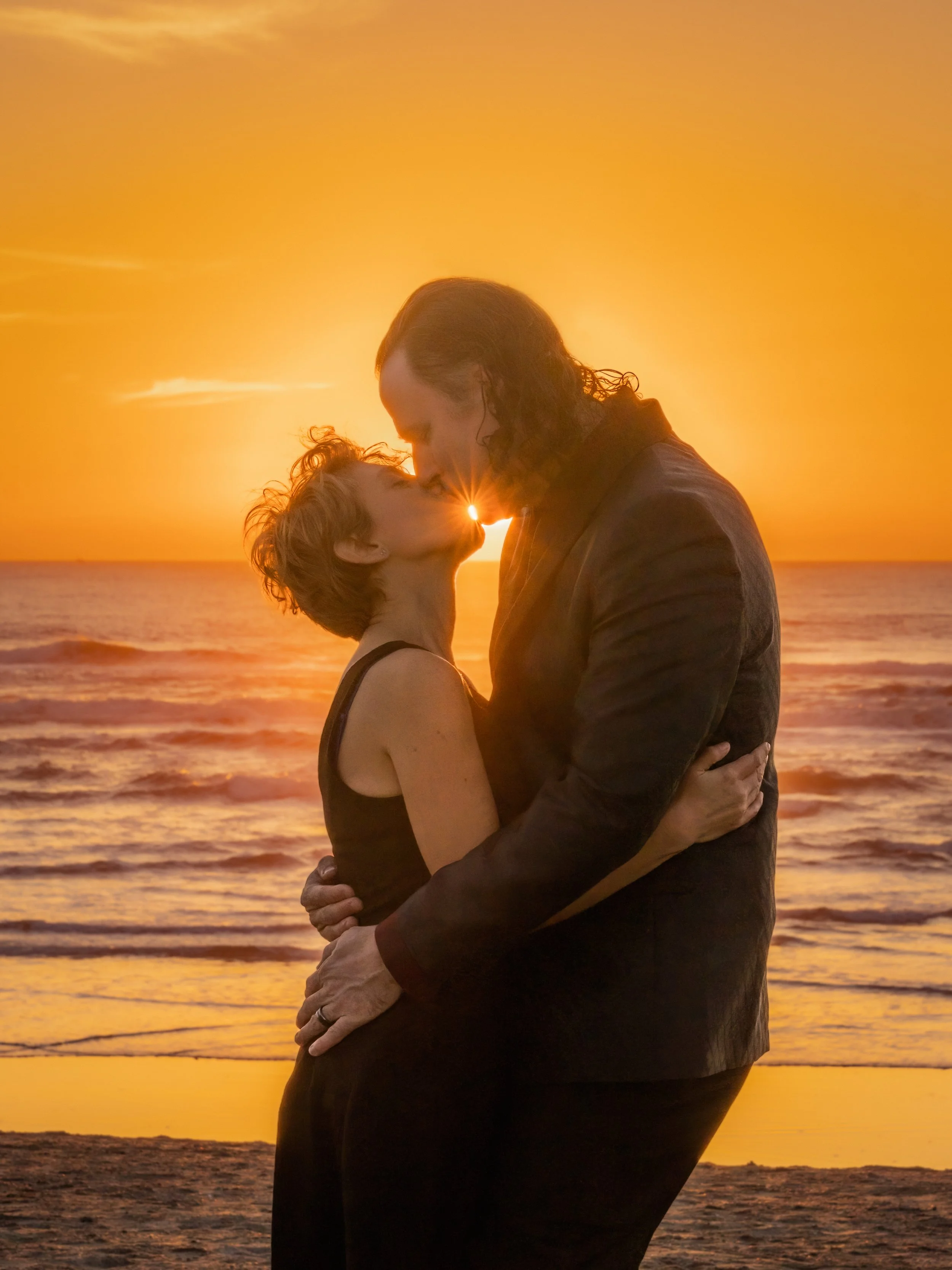A couple embracing and kissing on the beach at sunset.