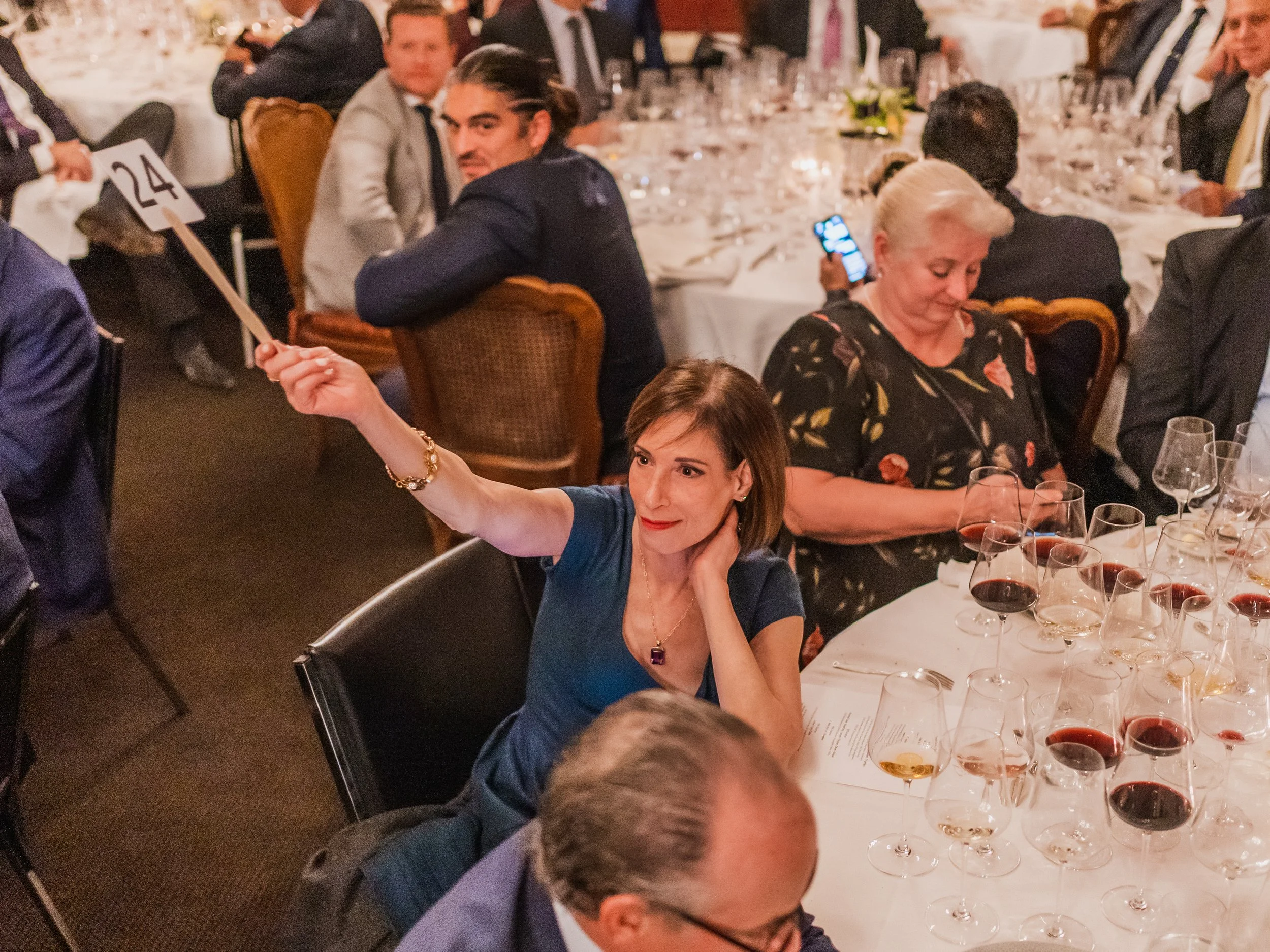 Woman in blue dress taking a selfie at a formal dinner event with multiple glasses of red and white wine on the table.