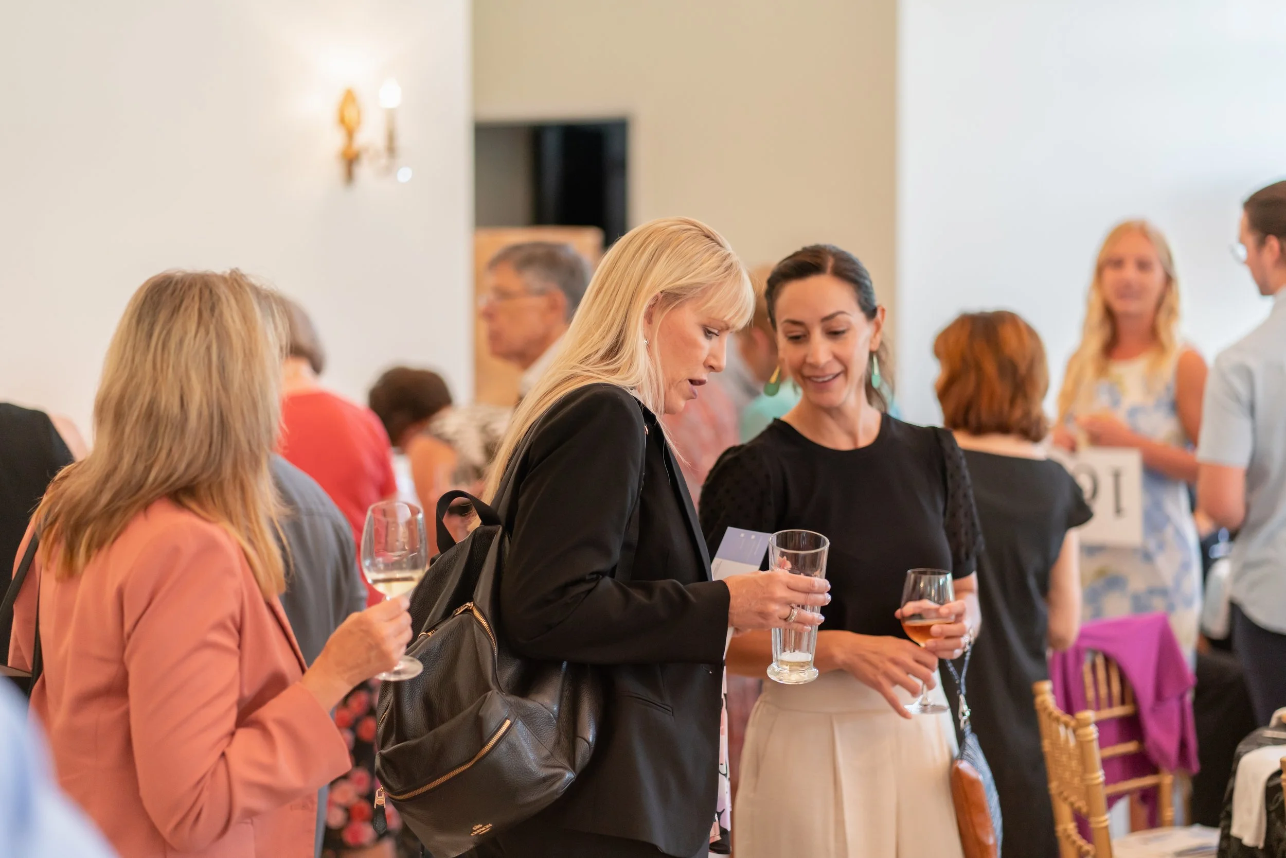 Group of women at a social gathering, holding drinks and engaging in conversation.