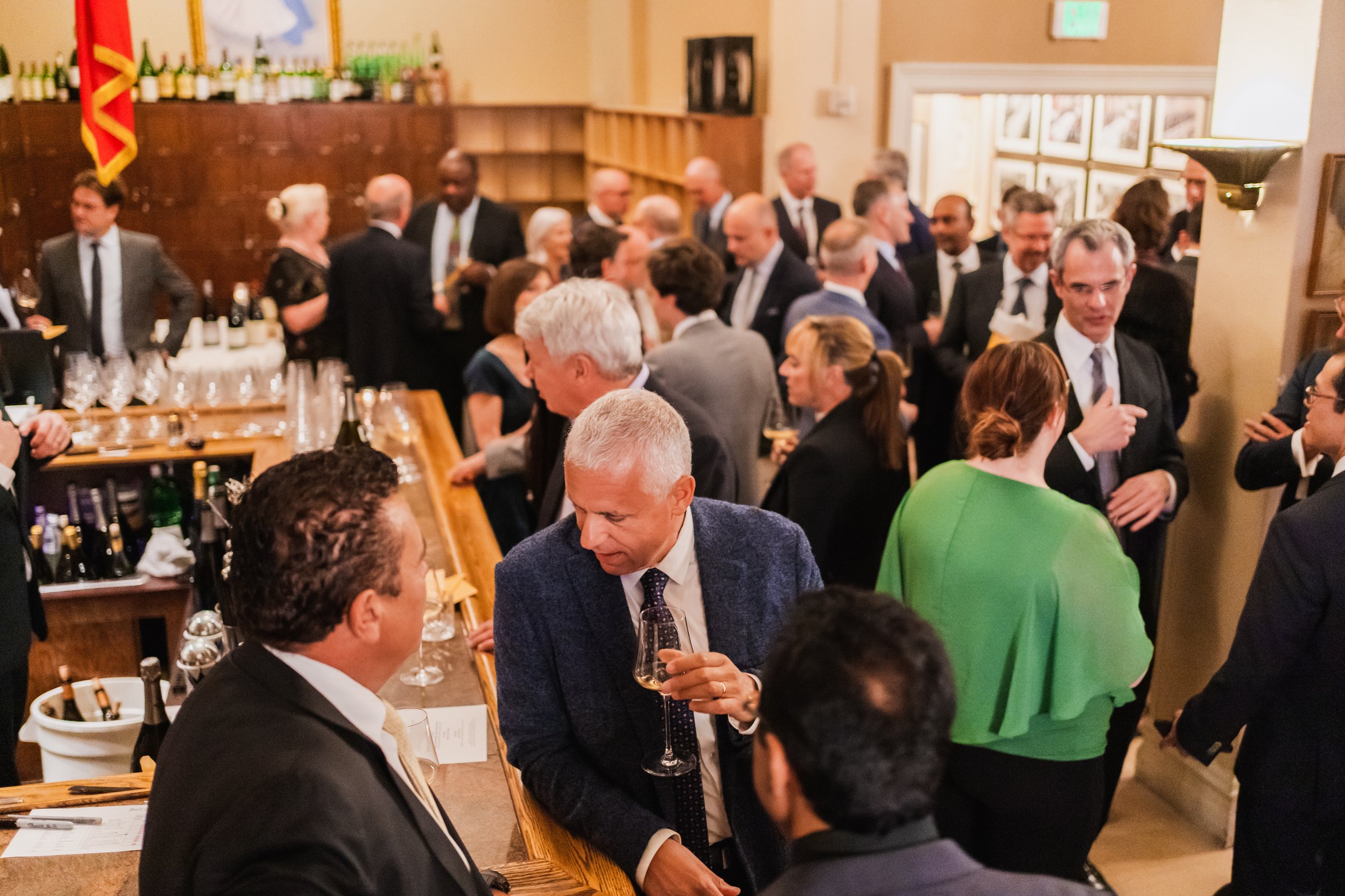 People socializing at a formal event or reception in an indoor venue with wooden decor and framed pictures on the wall.