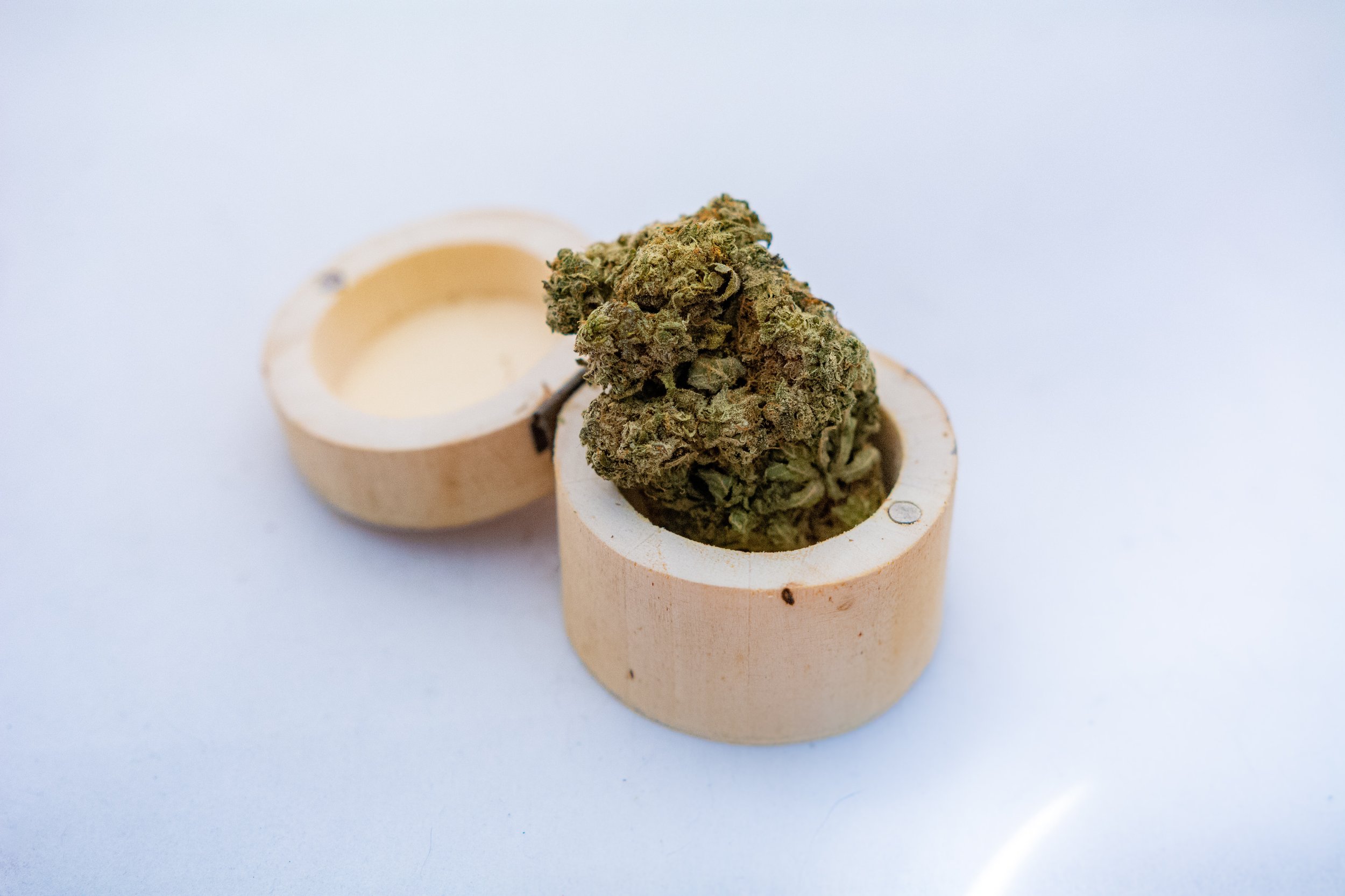 A cannabis bud inside a hollowed-out, circular wooden container, with another similar container in the background.