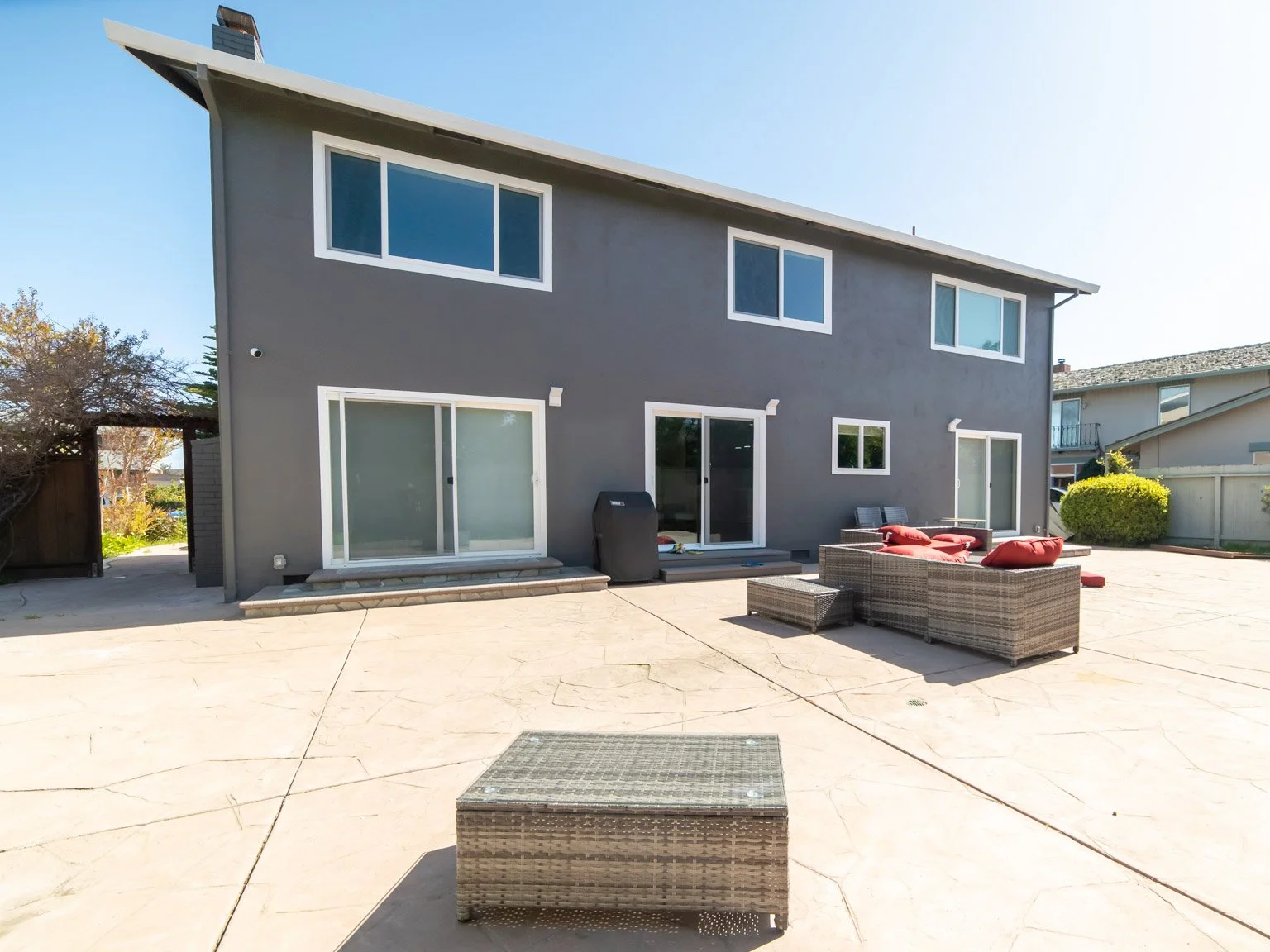 Backyard patio with wicker furniture and a dark gray house with large windows.