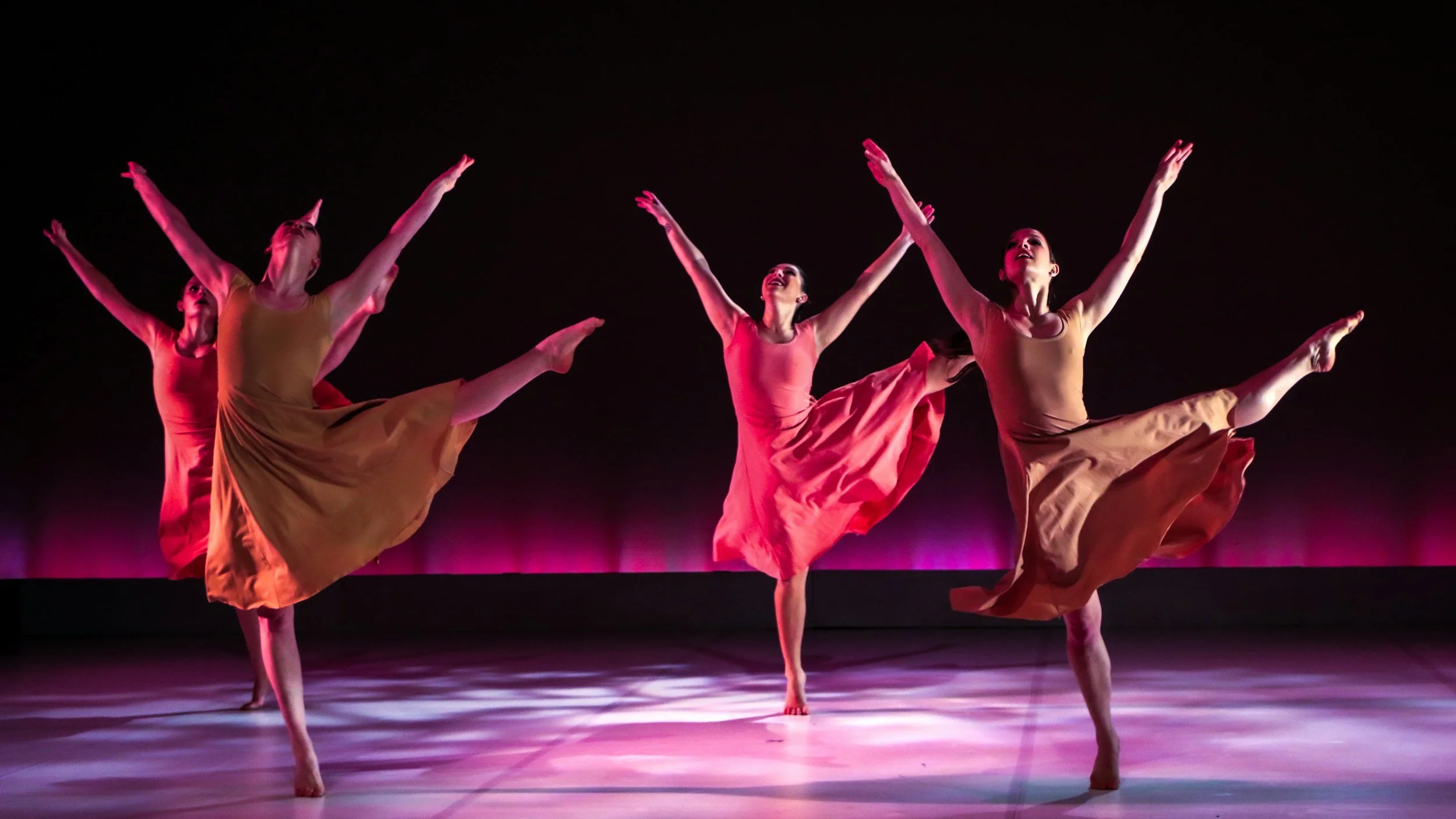 Ballet dancers in white tutus performing on stage with their arms raised.