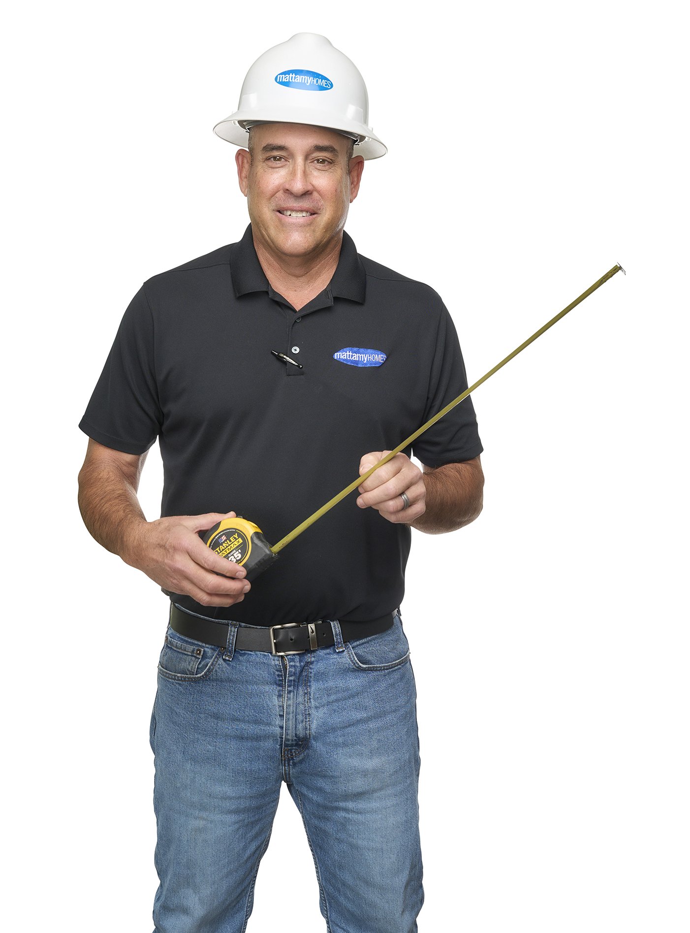 A man wearing a safety helmet and a black polo shirt with 'Mattamy Homes' logos, holding a tape measure and standing against a plain white background.