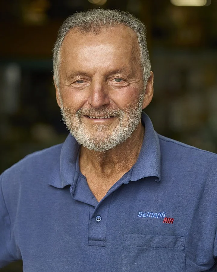 A smiling elderly man with gray hair and a beard, wearing a blue polo shirt with a logo that says 'Demand Air'.