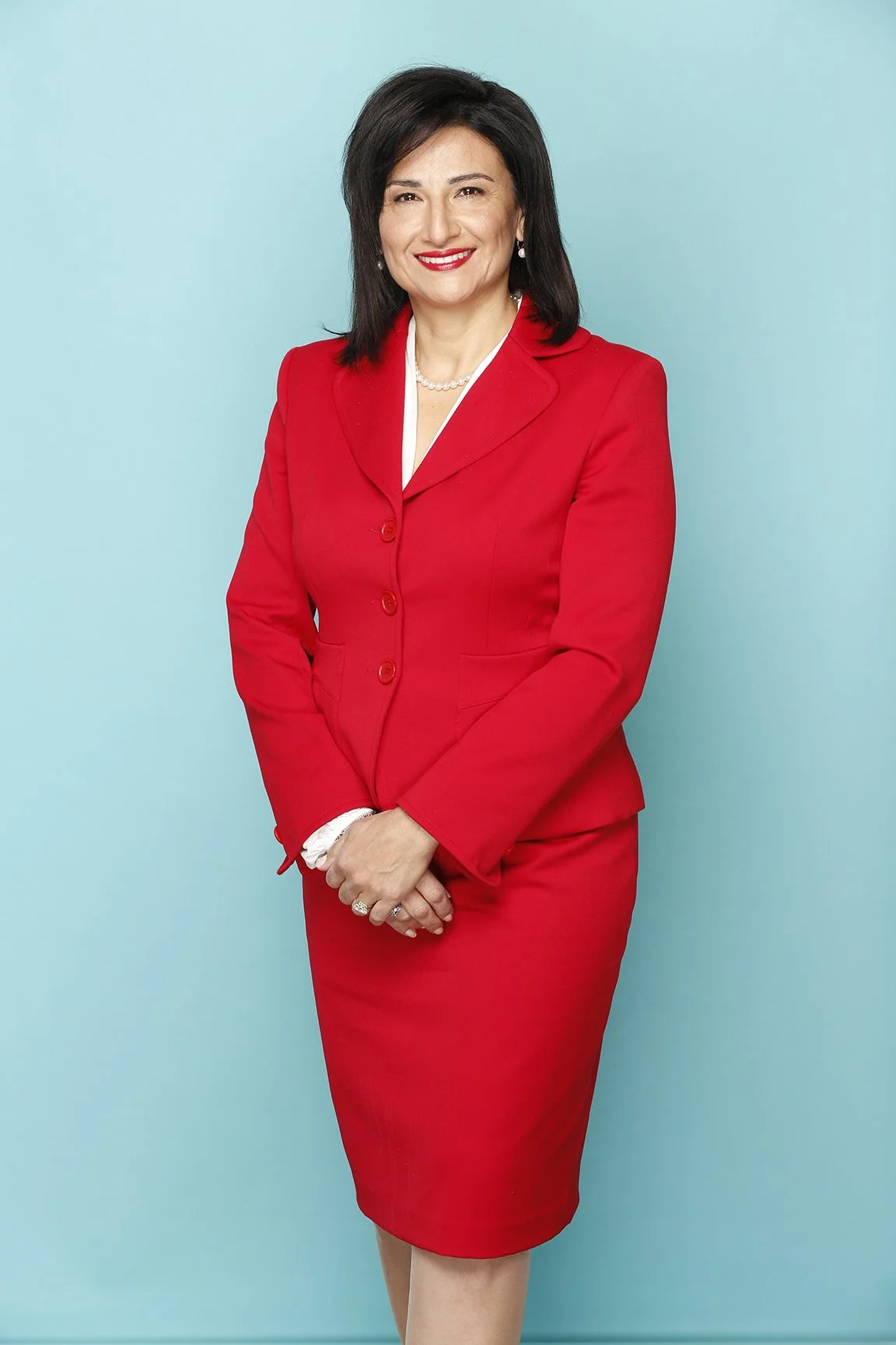 A woman in a red blazer and skirt, smiling, standing against a light blue background.