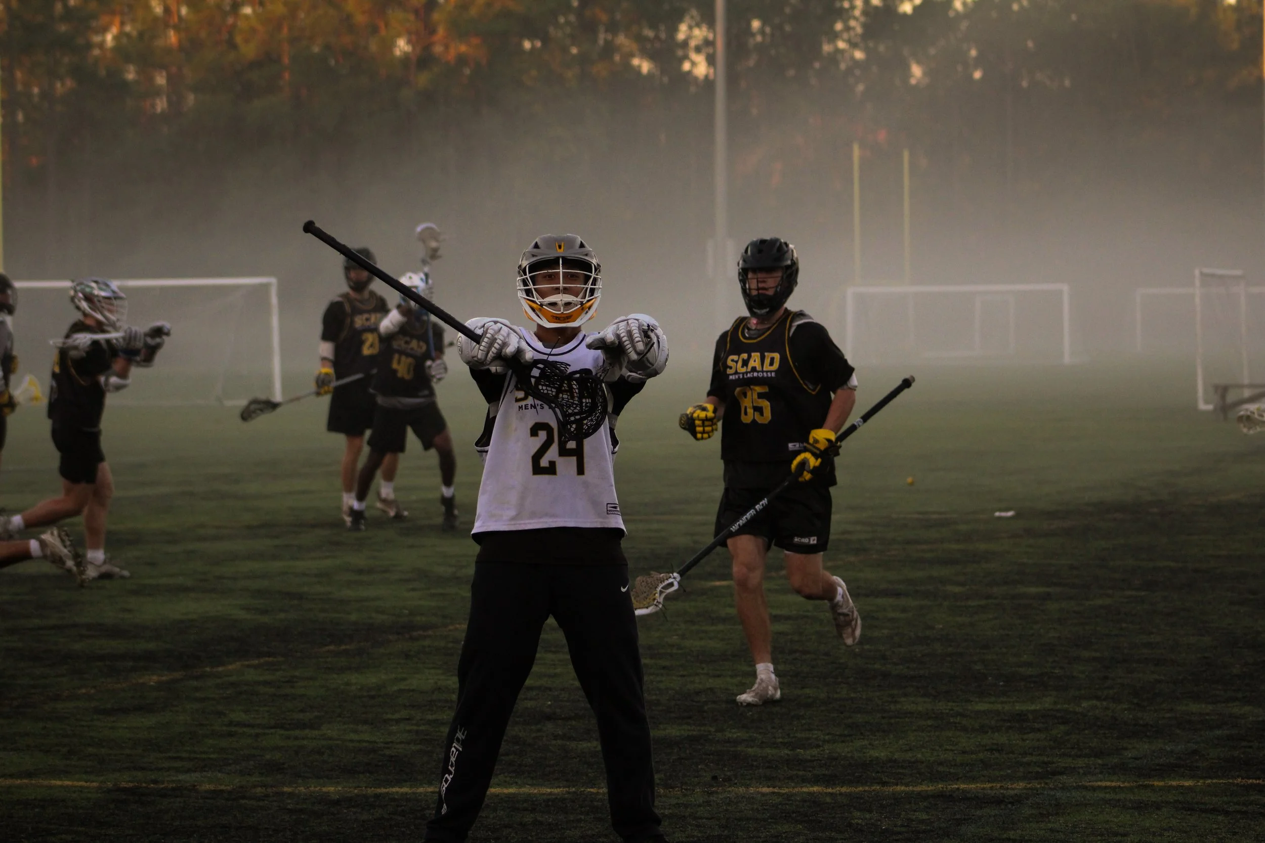 Lacrosse players practicing on a foggy field during sunset, with goal posts in the background.