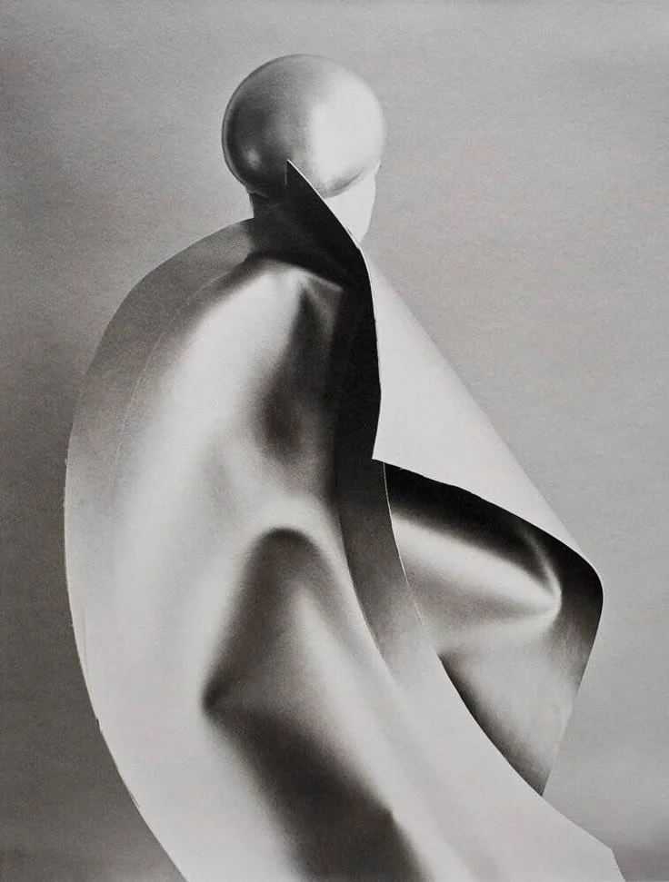 Abstract black and white sculpture of a seated figure with a smooth, shiny surface and a large folded paper accent.