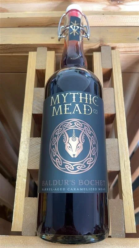 Bottle of Mythic Mead Baldwin's Bochet barrel-aged caramelized mead on wooden shelf.