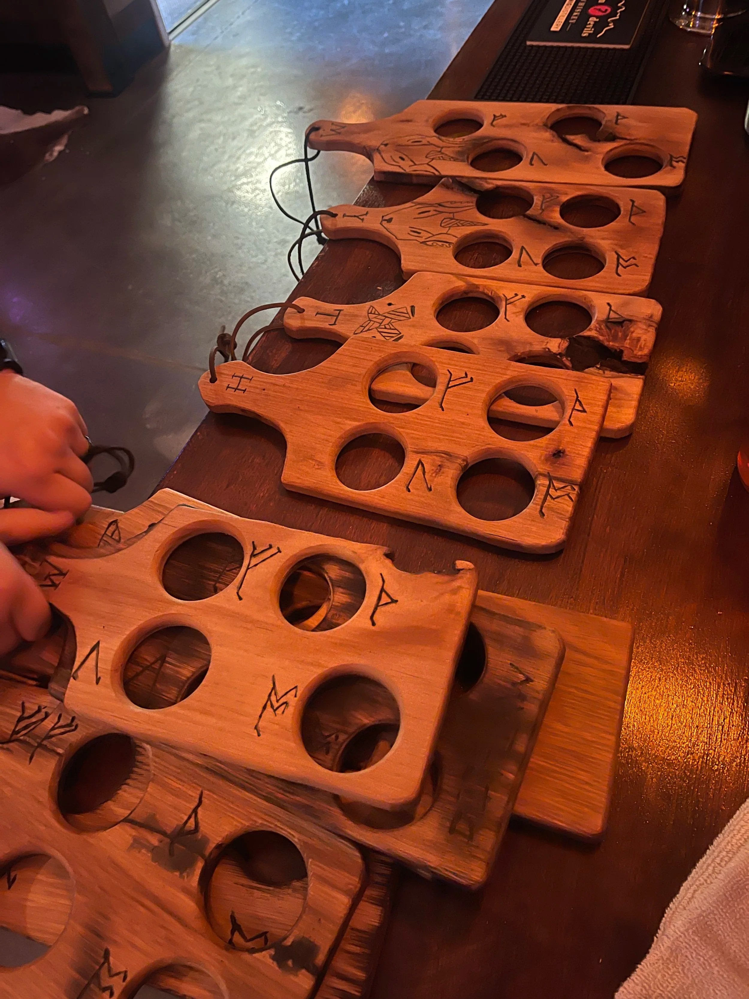 A row of wooden game boards with large circular cutouts and Viking runes inscribed around the edges, laid out on a wooden table in a bar or restaurant setting.