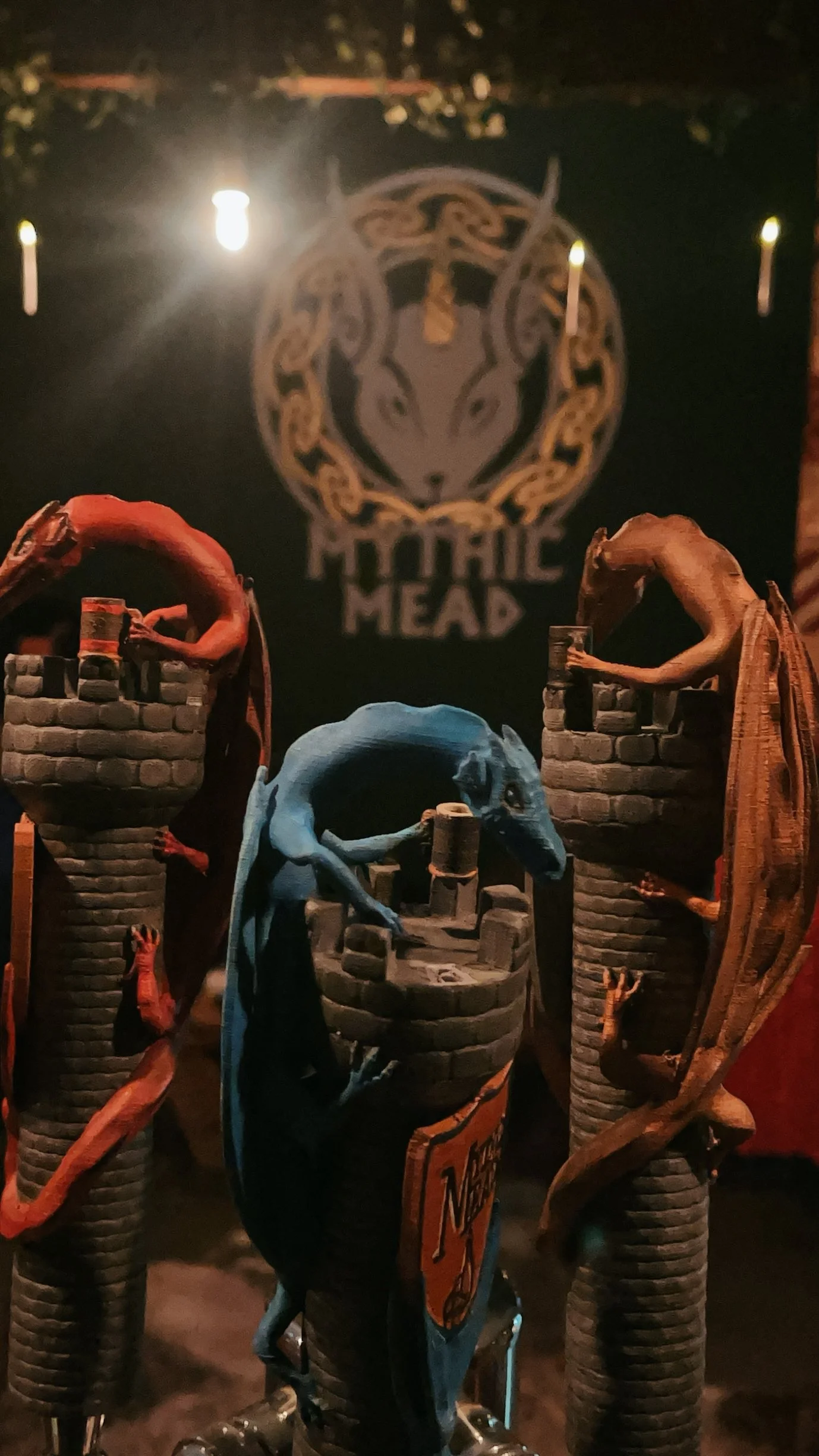 Close-up of motorcycle handlebar with three decorative grips featuring dragon figures twisting around them, with a background logo of a ram's head and the text 'Horrific Head' on a dark wall.