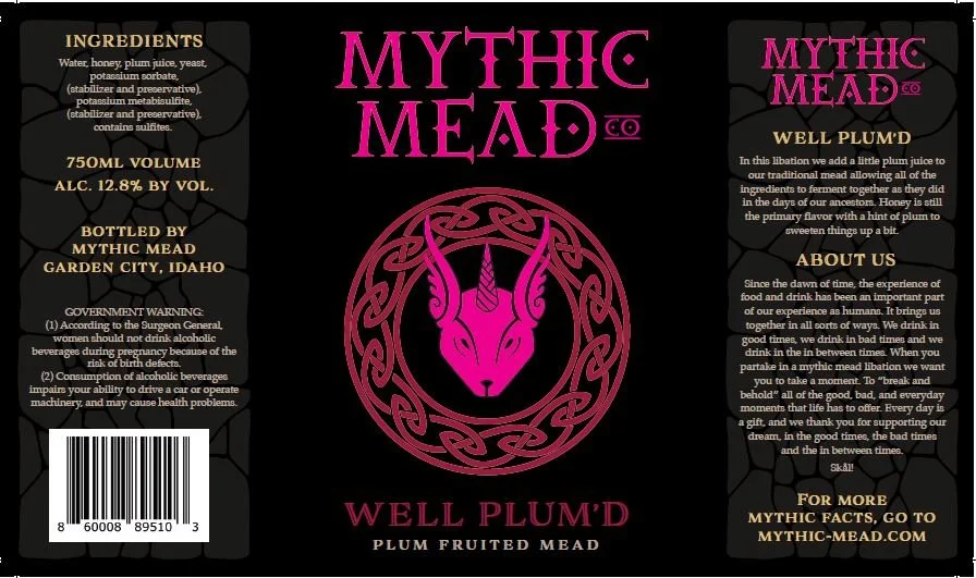 Black beverage label with pink and gold text, featuring a stylized goat head logo. Contains ingredients, alcohol content, volume, origin, government warning, company information, and a description of the mythic mead called Well Plum'd.