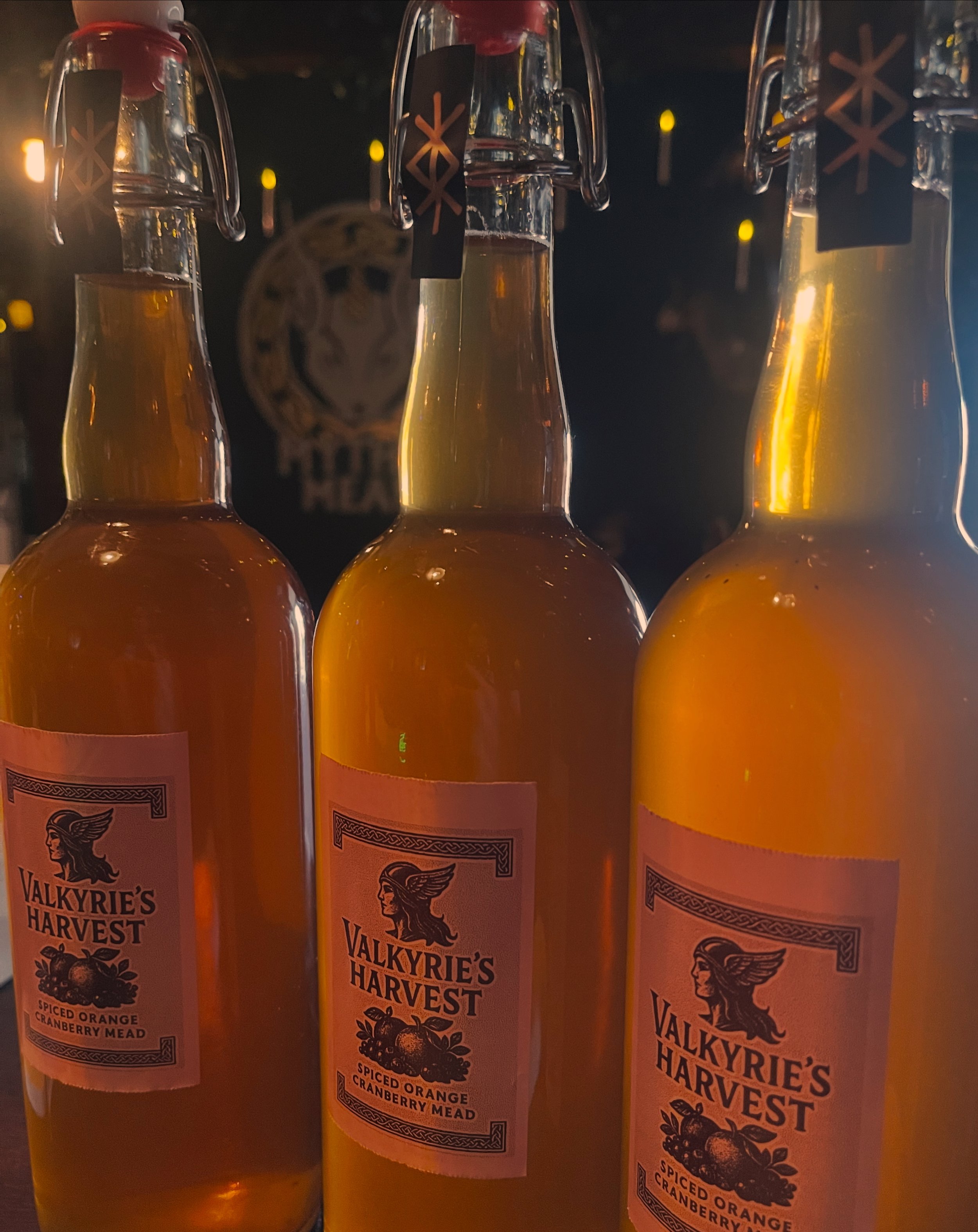 Three glass bottles of Valkyrie's Harvest spiced orange cranberry mead on a shelf.
