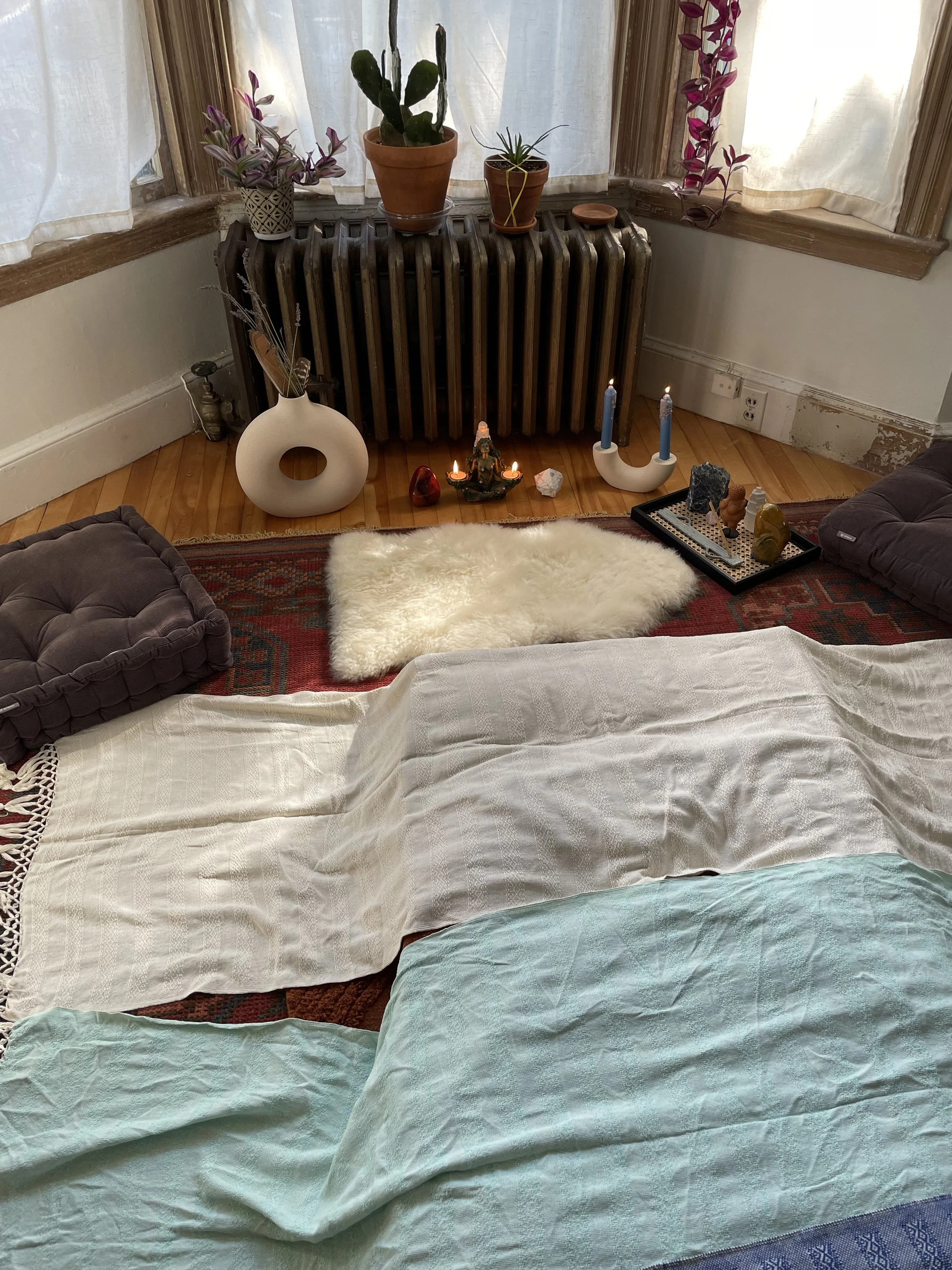 A cozy living room corner with a bed and various decorative items, including plants, candles, and a fountain.