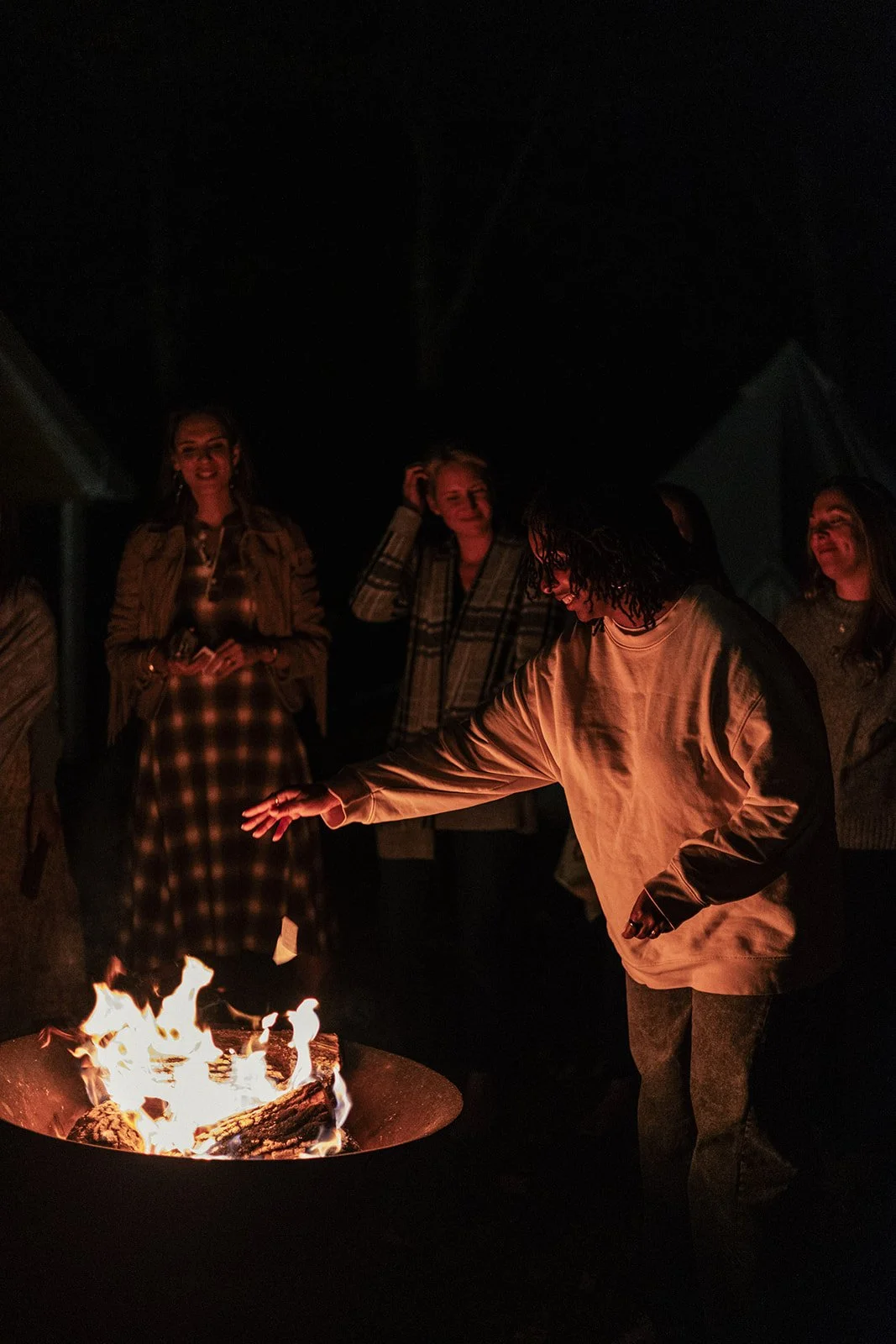People gathering around a campfire at night, smiling and enjoying the moment.