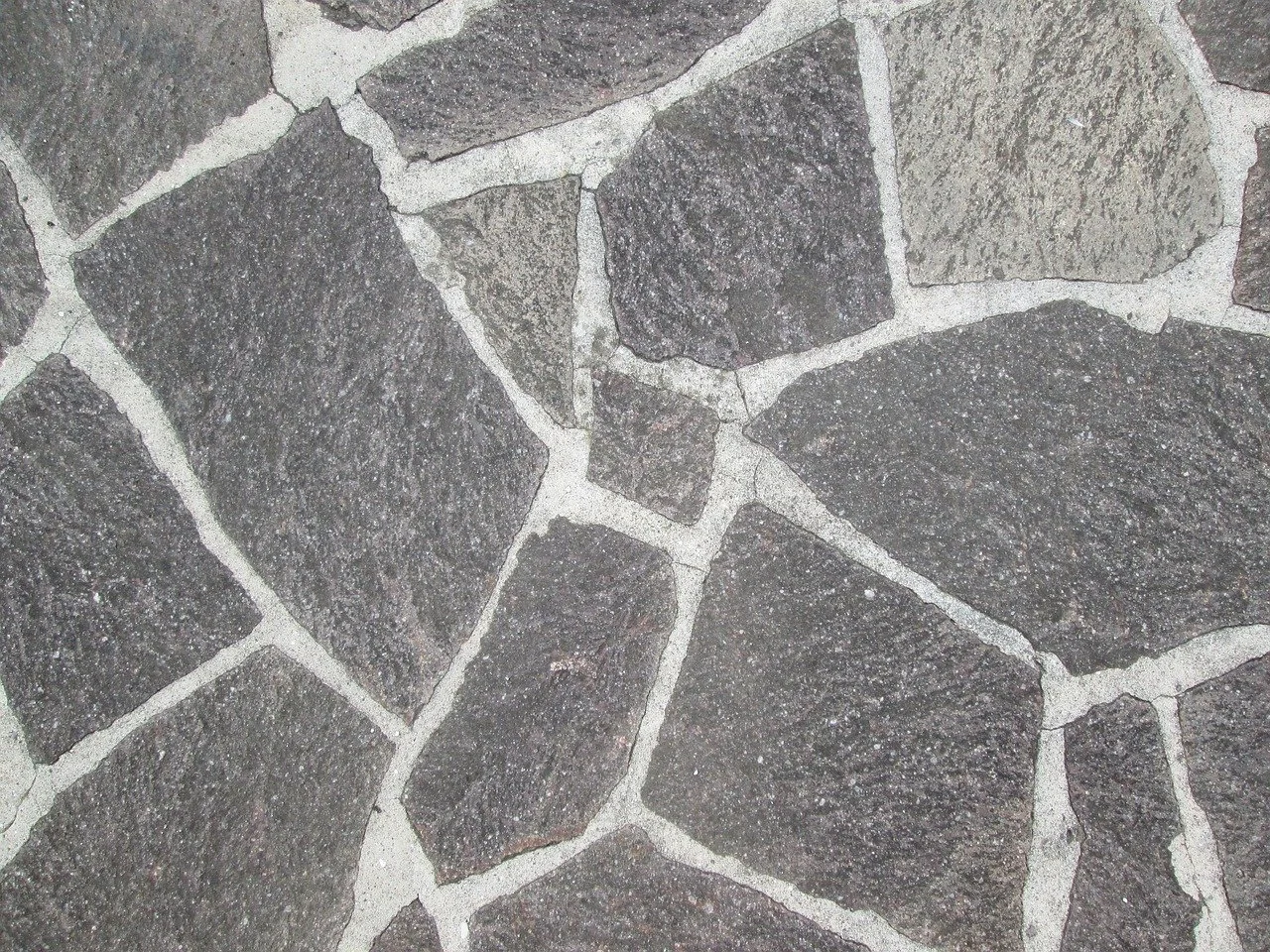 Close-up of irregularly shaped dark gray and brown stone tiles with white grout lines.
