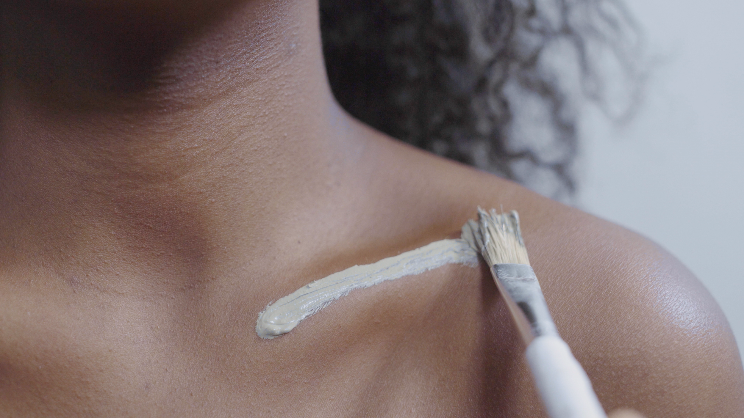 Close-up of a person applying white cream to the skin on their shoulder with a small brush.