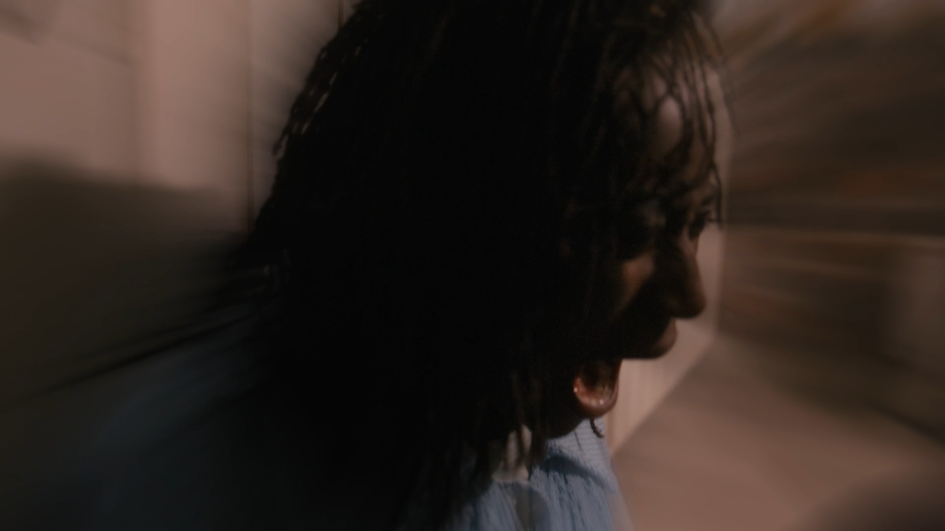 Person with curly hair leaning against a wall with blurred motion effect.