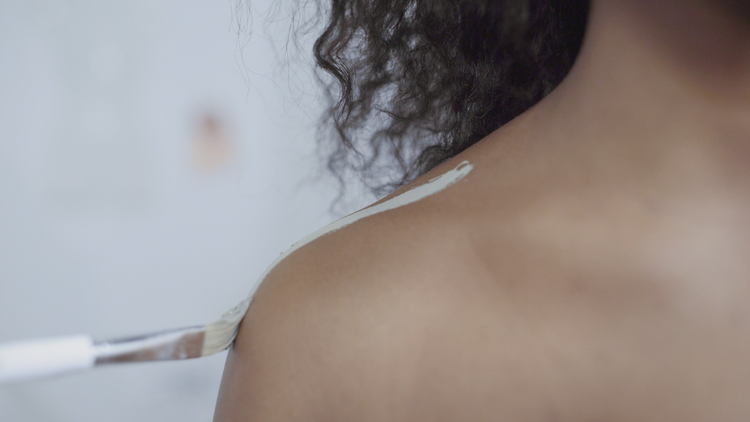 Close-up of a person applying white paint on their shoulder with a paintbrush.