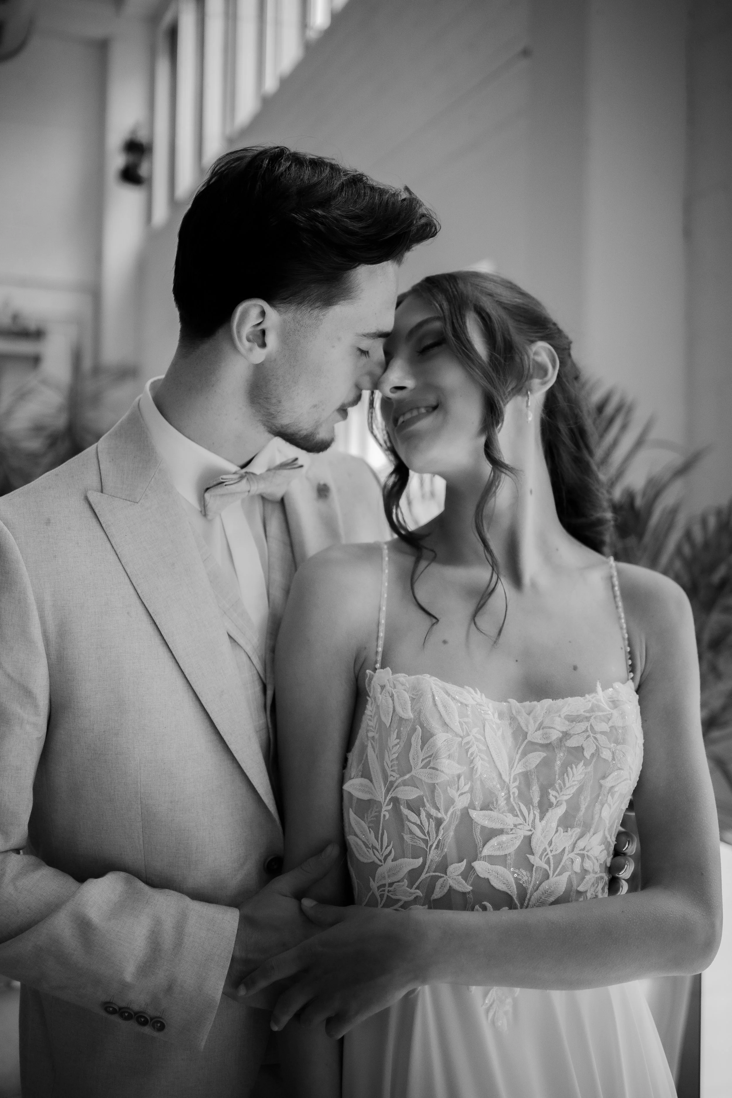 Ein glückliches Brautpaar in formeller Kleidung, das sich liebevoll berührt, in Schwarz-Weiß-Fotografie.