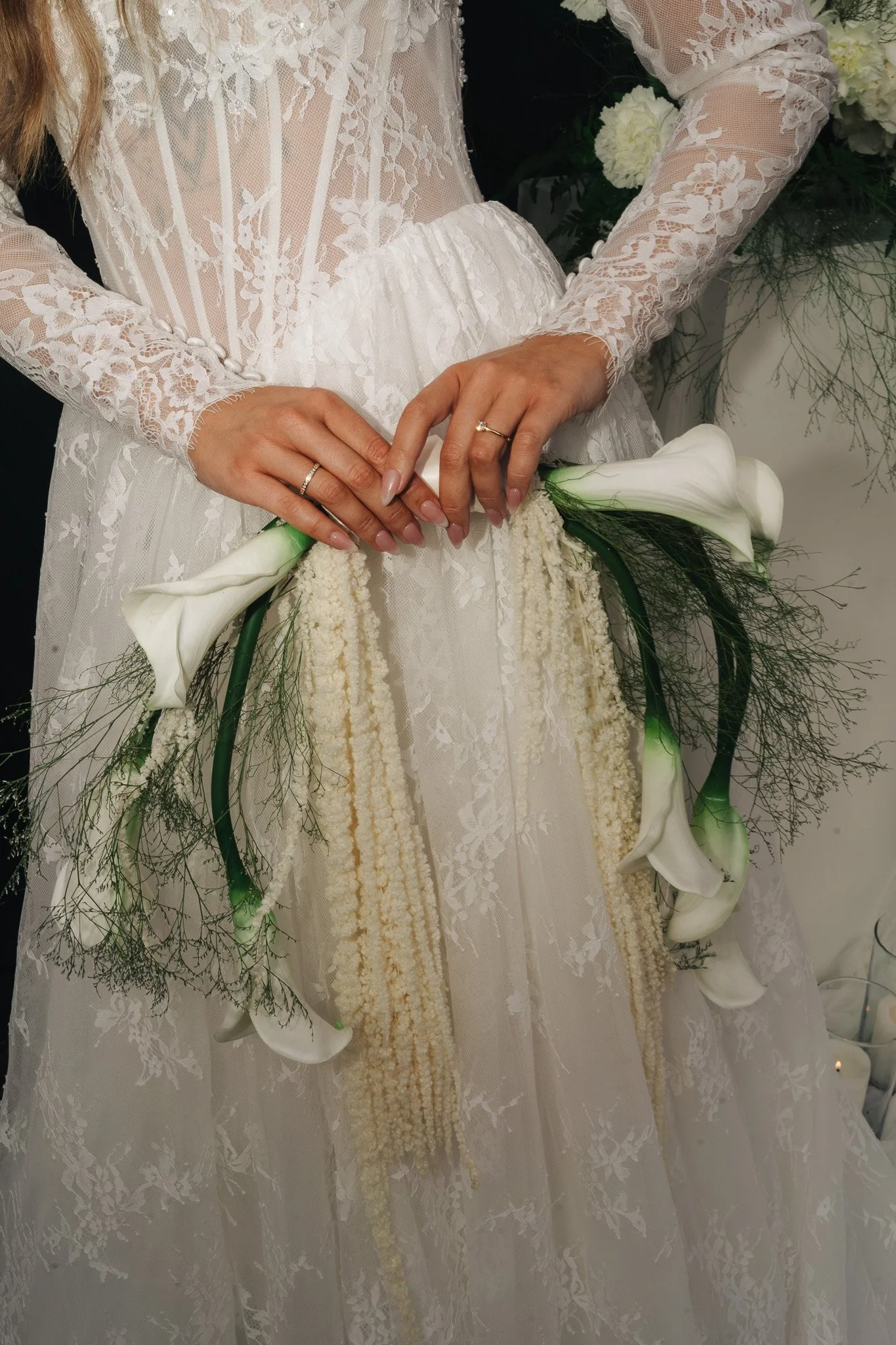Braut in weißem Spitzenkleid mit ihren Händen, die Ringe tragen, hält einen weißen Blumenstrauß mit Calla-Lilien.