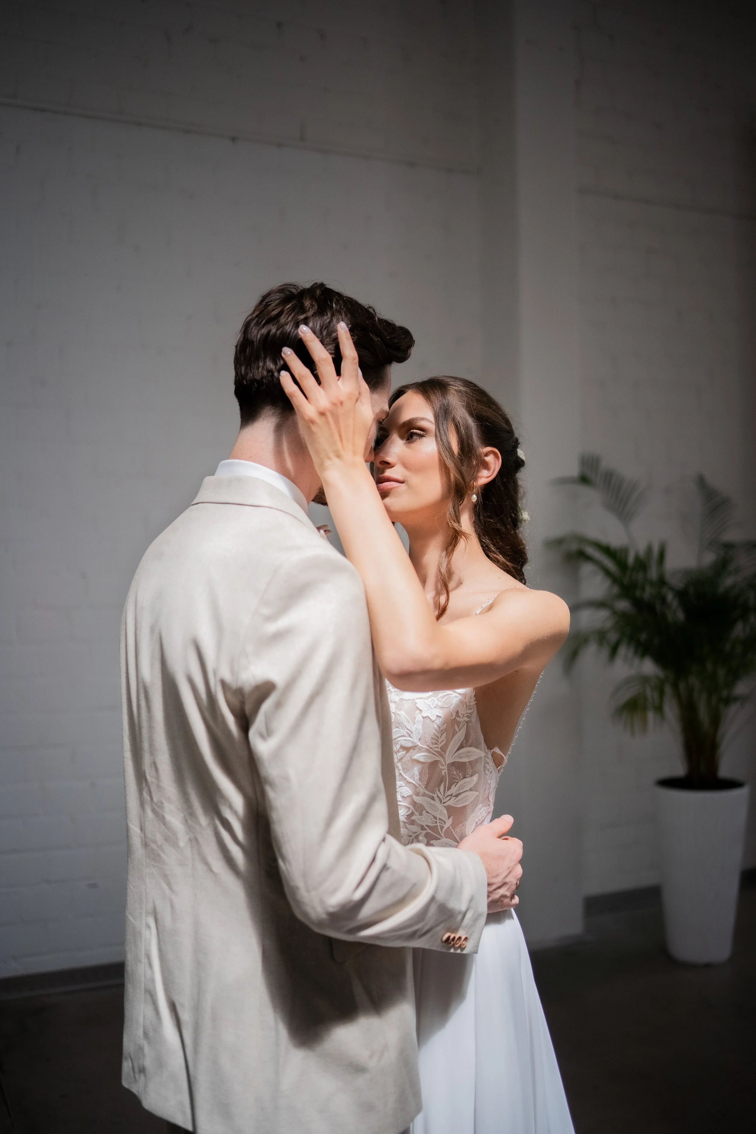 Ein Hochzeitspaar, das sich innig umarmt, in einem weißen Raum mit einer Topfpflanze im Hintergrund.